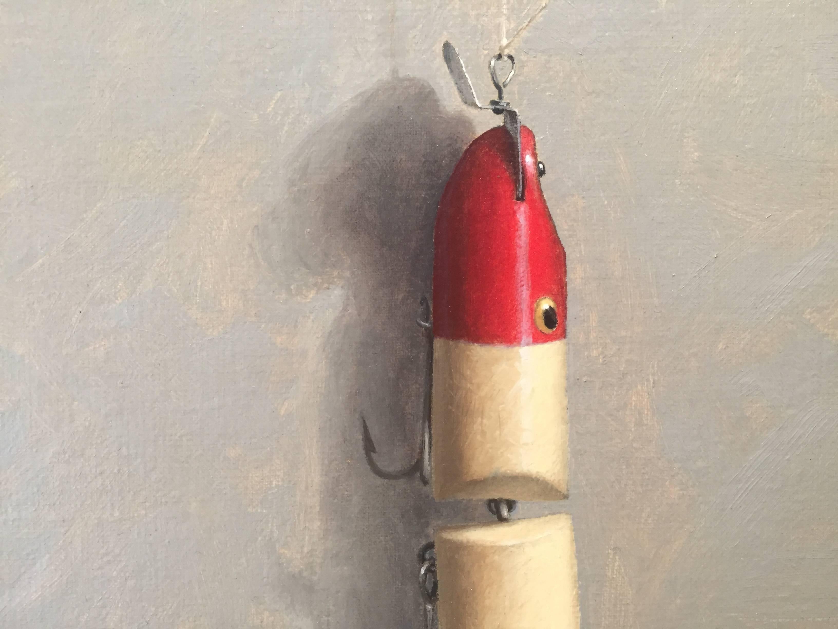 Painted from life in his Connecticut studio, a red and white 2-piece fishing lure hangs from a tiny metal nail. A thin white thread hooks the lure to the nail, 3 anchor-like hooks dangle from the lure, pointed sharp and glistening in rustic charm.