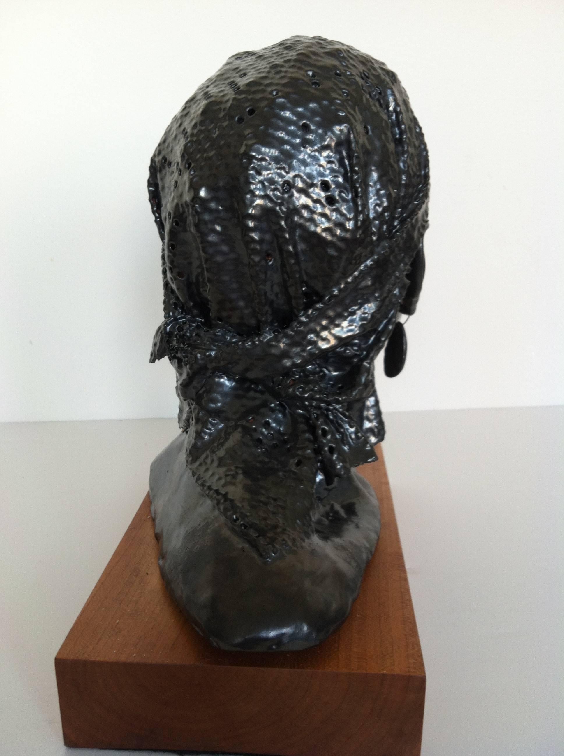 This is a life size-head of the iconic singer Nina Simone, sculpted in ceramic and covered in a taupe/silver metal glaze. The bust stands on a pedestal of cherry.
Thick tear drop earrings hang from her ear lobes.The head is covered by an