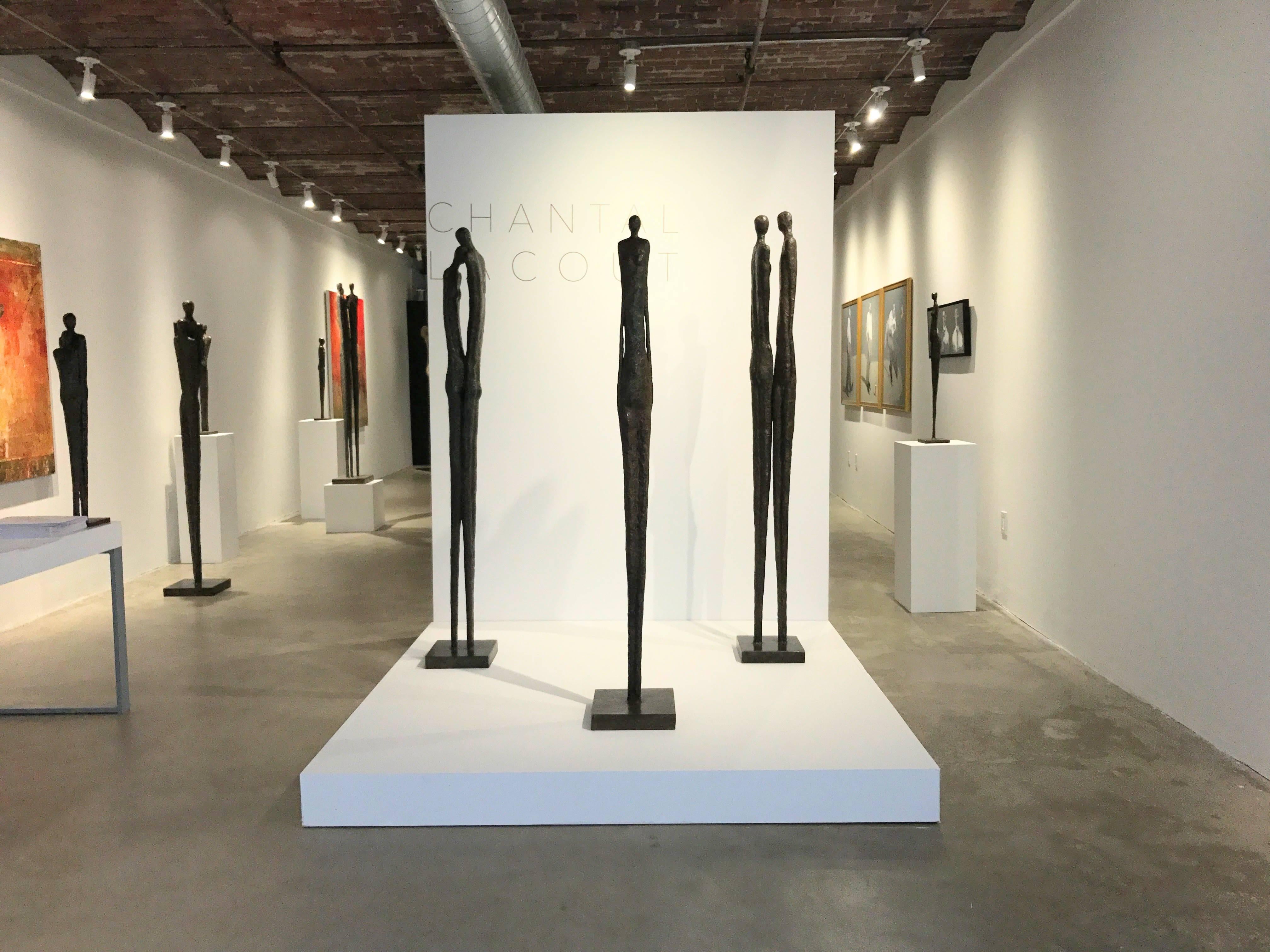 This contemporary bronze sculpture renders three human figures in a line, tall, long, and elegant. Though minimal in detail, this modern sculpture creates a strong relationship between the three figures with using their posture and placement to