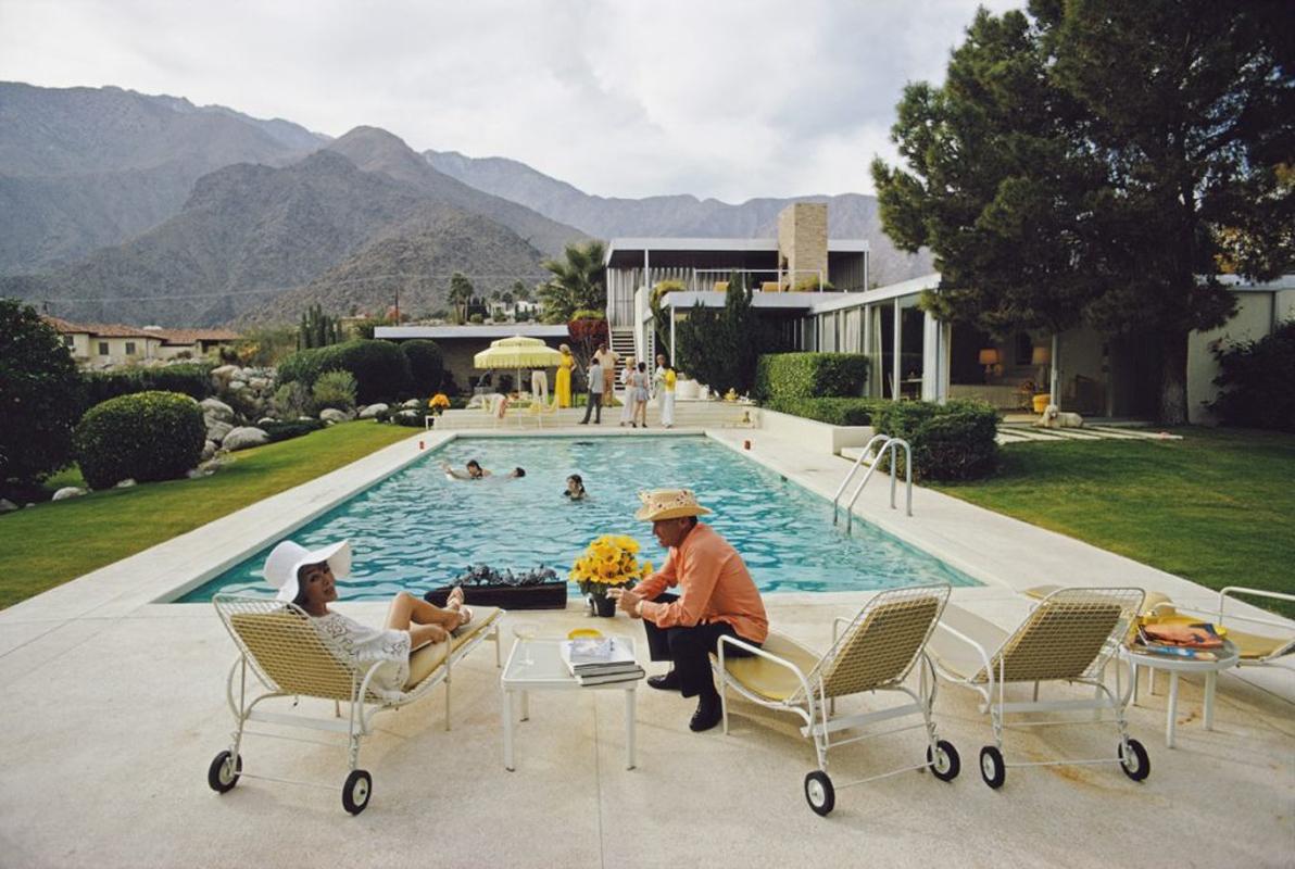 Slim Aarons Estate Limited Edition C print 60 x 40" inches unframed.

' Kaufmann Desert House '

Lita Baron talking with a guest at a poolside party at Nelda Linsk’s desert house in Palm Springs, California, January 1970. The house was designed by