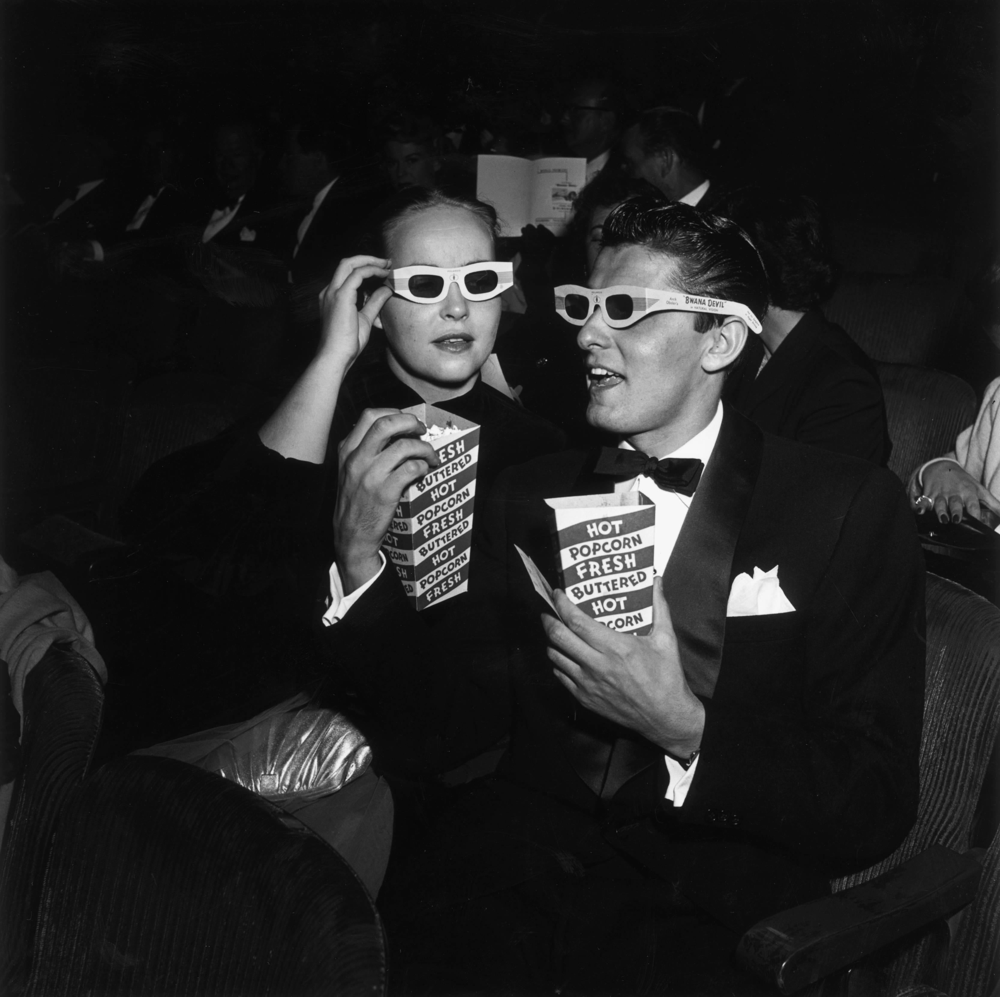 November 1952: EXCLUSIVE American actor Keefe Brasselle and his wife Norma, wearing 3-D glasses and holding boxes of hot buttered popcorn, sit in the theater at the premiere of director Arch Oboler's film, 'Bwana Devil,' Hollywood, California. The