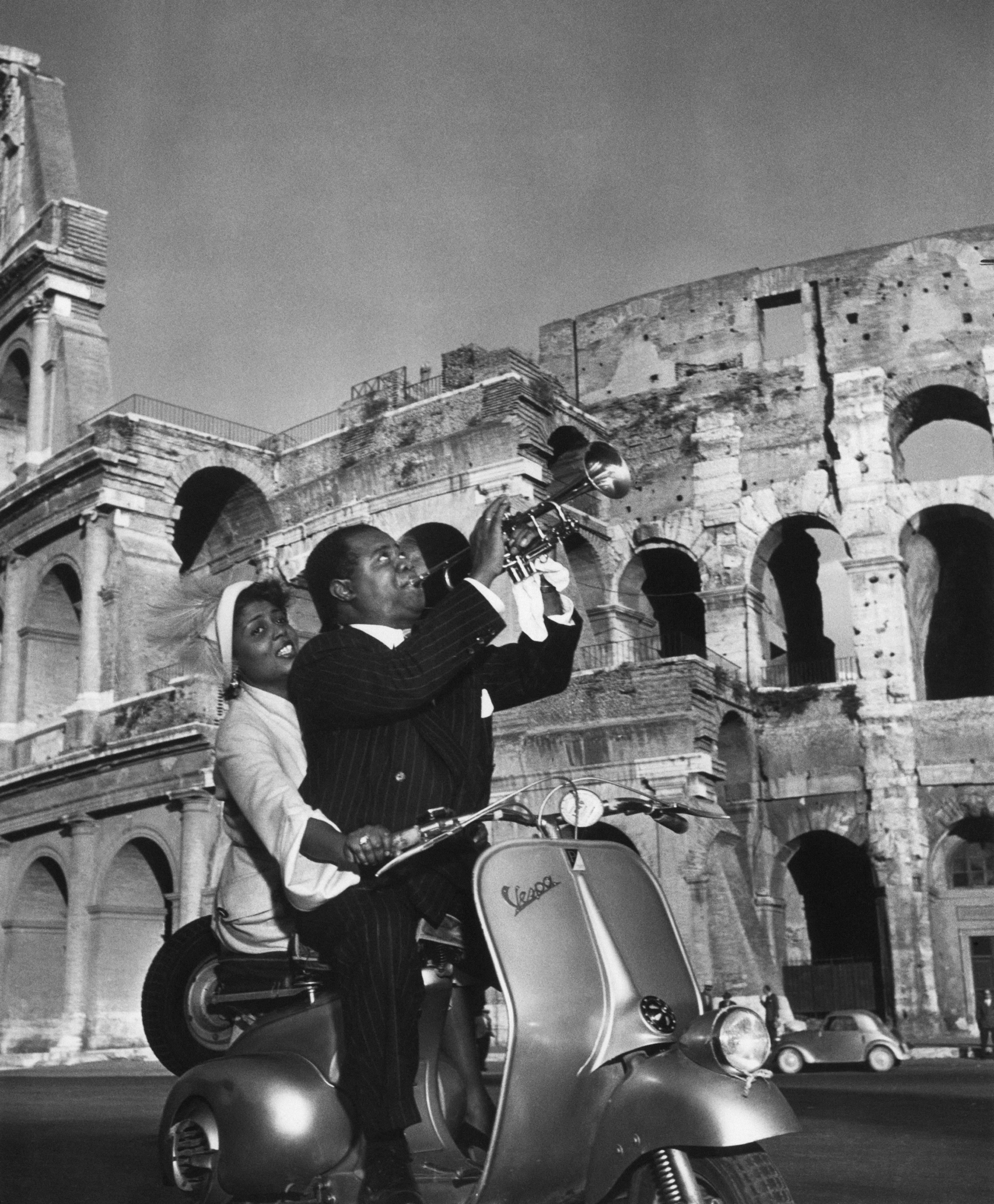 Lucille Brown takes control of the Vespa scooter as her husband Louis Armstrong (1898 - 1971) displays his musical appreciation of the ancient Colosseum in Rome. (Photo by Slim Aarons/Getty Images)

C-type print from the original transparency held