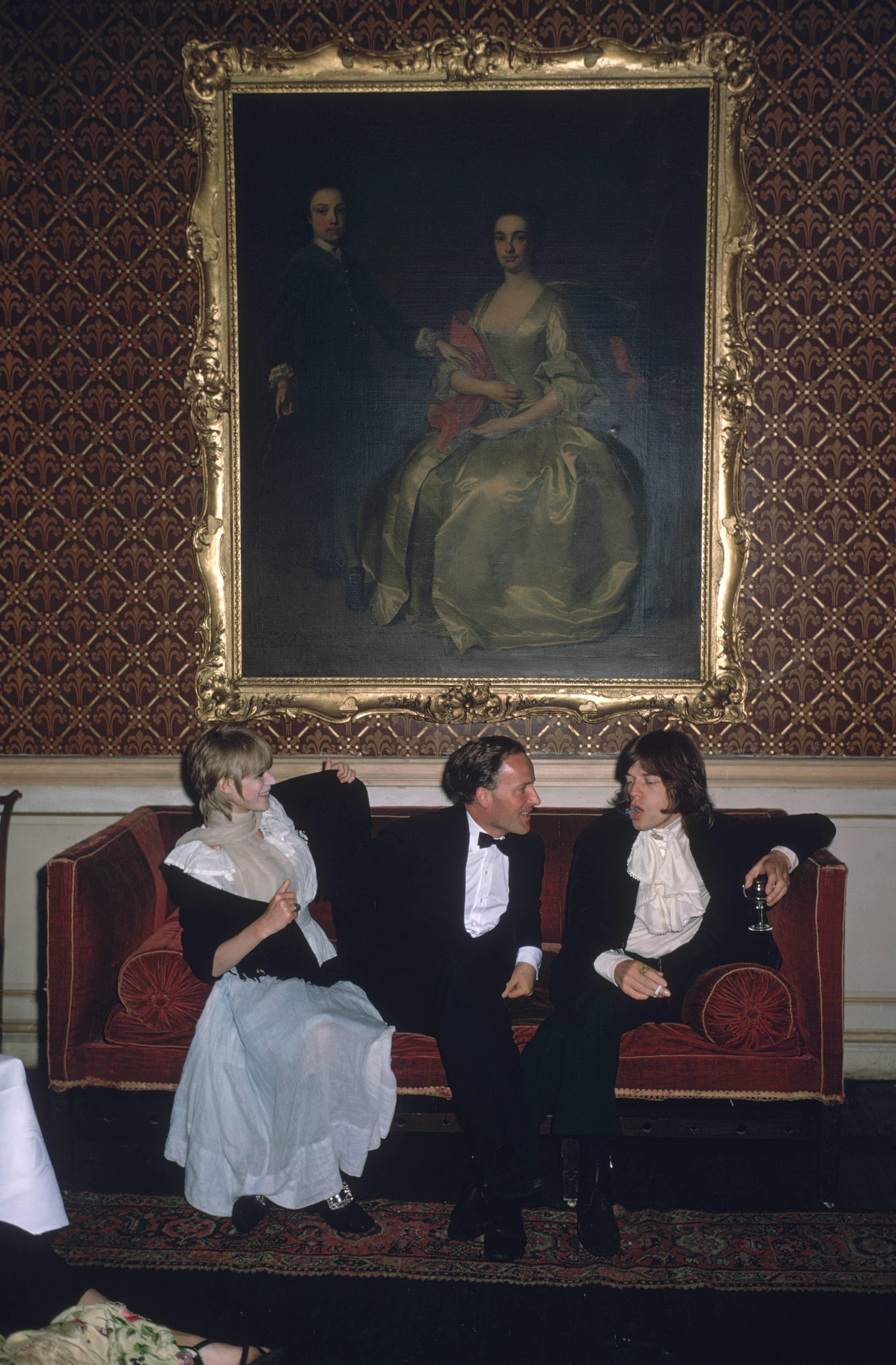 1968: From left to right; singer Marianne Faithfull, the Honorable Desmond Guinness and Mick Jagger (of the Rolling Stones) sit on a sofa under a large gilt framed painting of a woman in 18th century dress at Leixlip Castle, Ireland, the home of