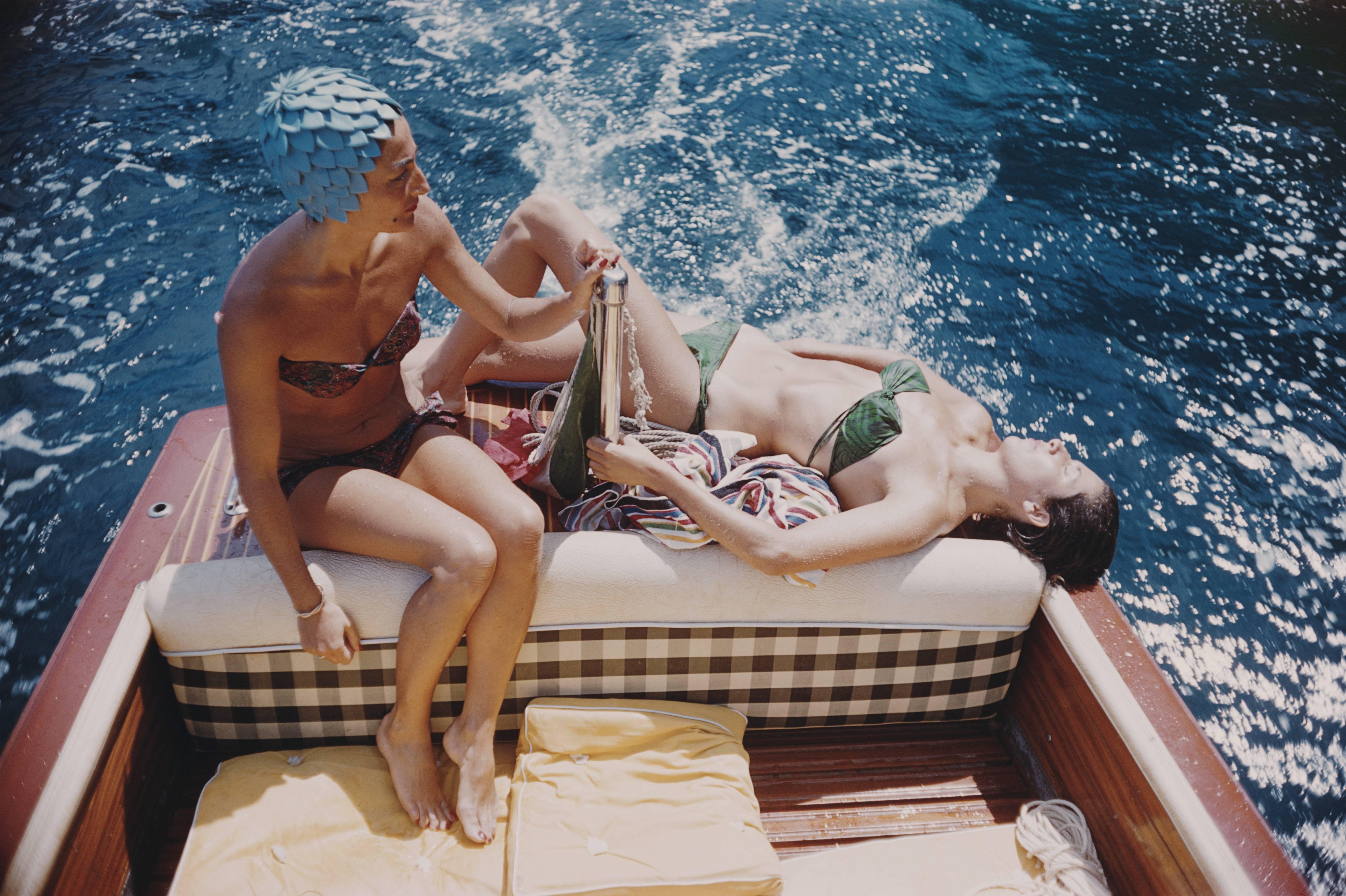 Carla Vuccino, wearing a swimming cap, and a sunbathing Marina Rava, both wearing bikinis as they sit on the rear of a boat, on the waters off the coast of the island of Capri, Italy, 1958 . (Photo by Slim Aarons/Getty Images)

C-type print from the
