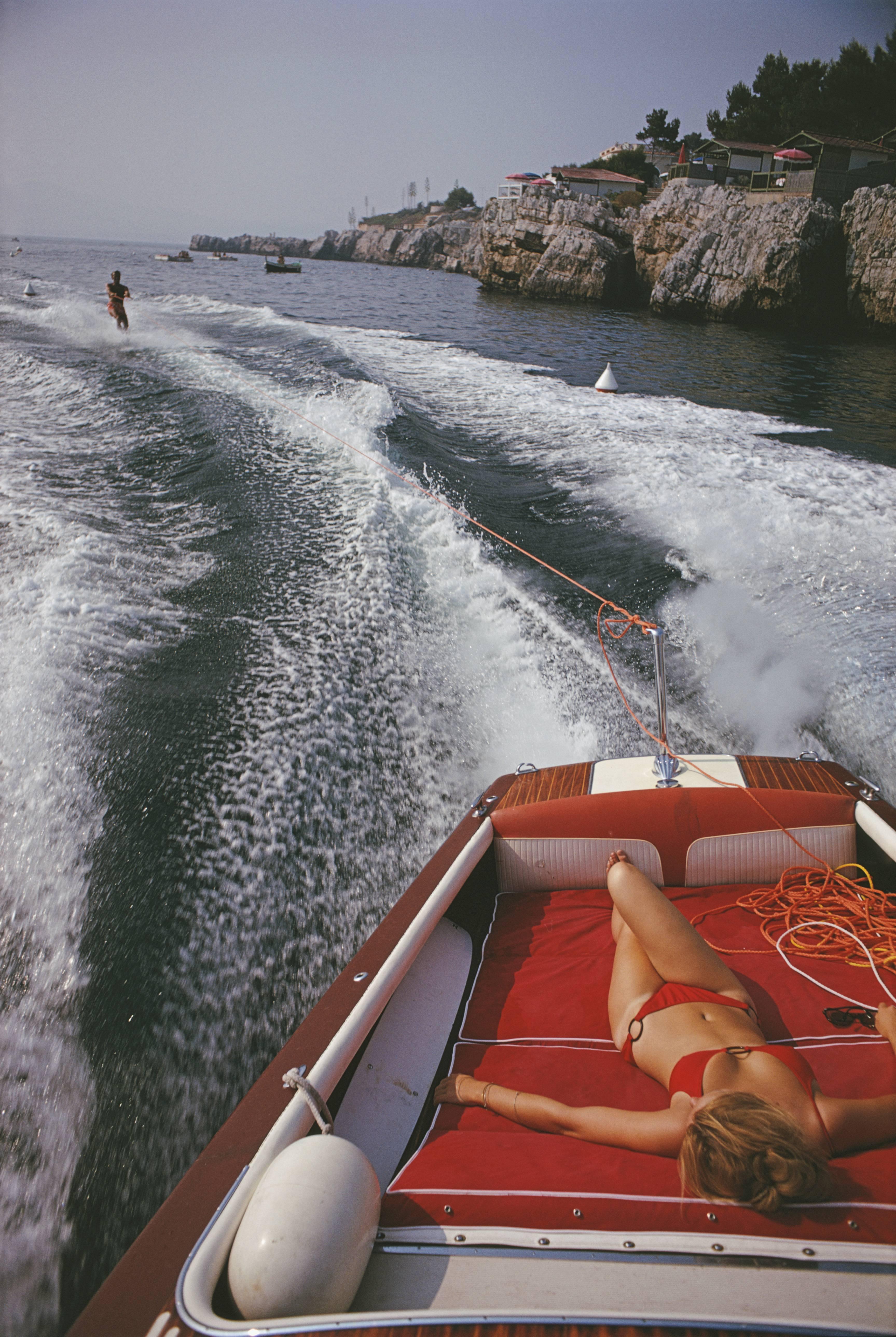 A woman sunbathing in a motorboat as it tows a waterskiier, in the sea off the Hotel du Cap-Eden-Roc in Antibes on the French Riviera, August 1969.

C-type print from the original transparency held at the Getty Images Archive, London.  Numbered and