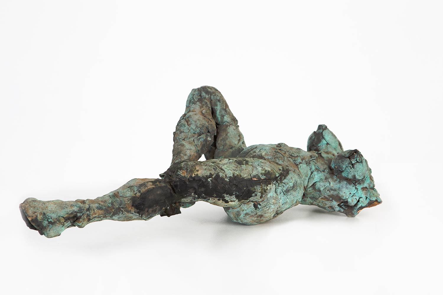 “Reclining” from 1985 is a patinated stoneware sculpture by Ruth Aizuss Migdal that depicts a reclining nude figure. The patina provides this piece with an exquisite range of color varying in greens and blues that contrast against the dark brown