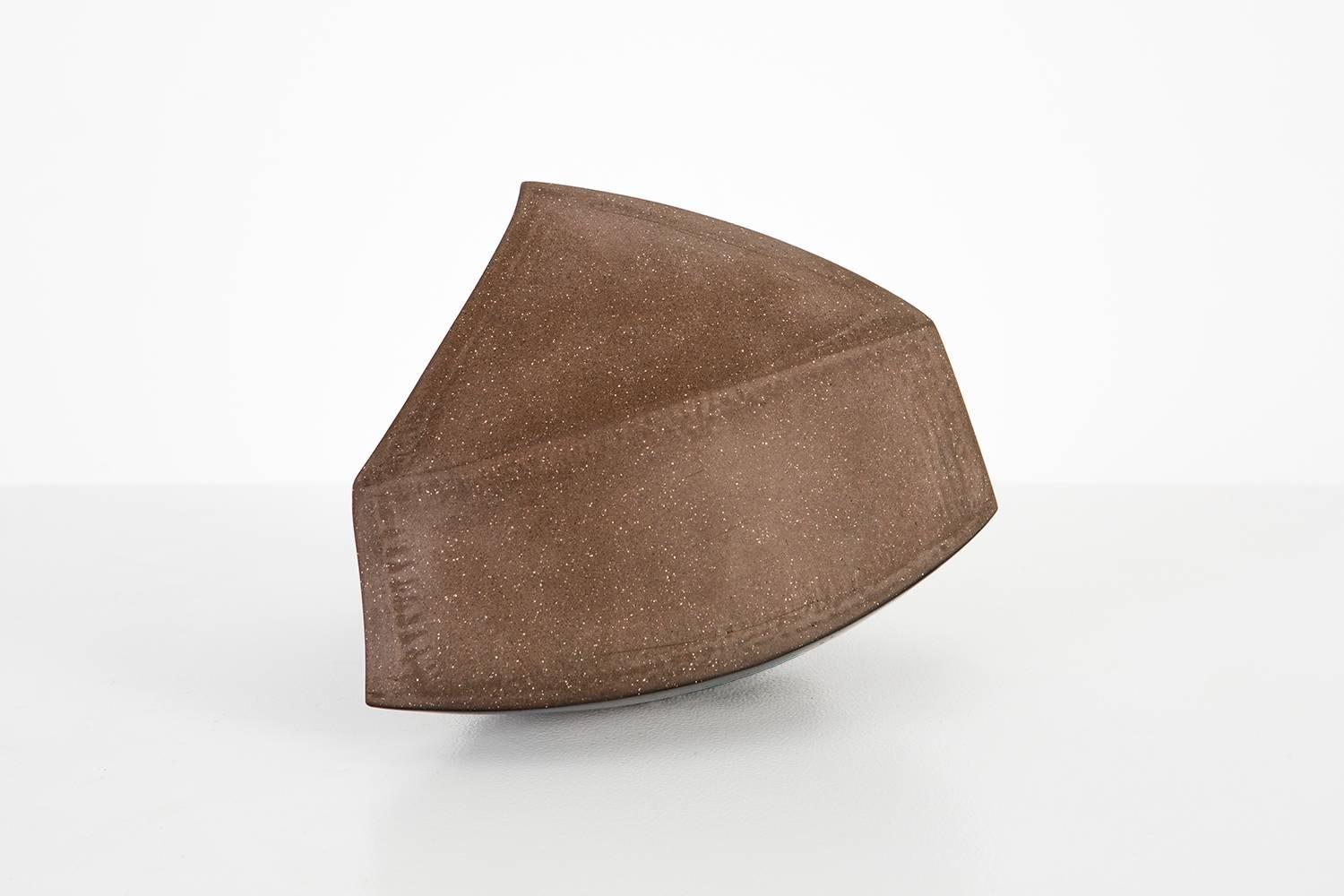 This partially glazed dark brown stoneware sculpture combines all the building block shapes of geometry. Depending on the point of view, this sculpture appears triangular, circular or square. Despite its geometric quality, it maintains an organic