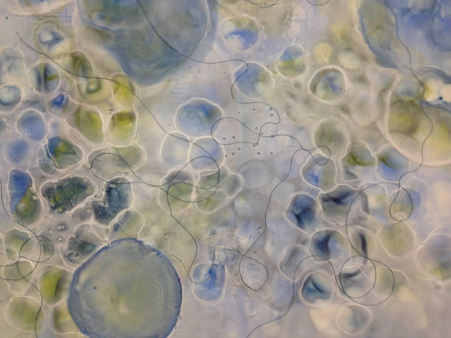 Kay Hartung’s “Bio Flow 3” is a 16 x 16 inch mixed media painting incorporating encaustic and pastel composed of microscopic images actively forming connections in blues, greens and whites, with actual thread embedded in the surface. The painting
