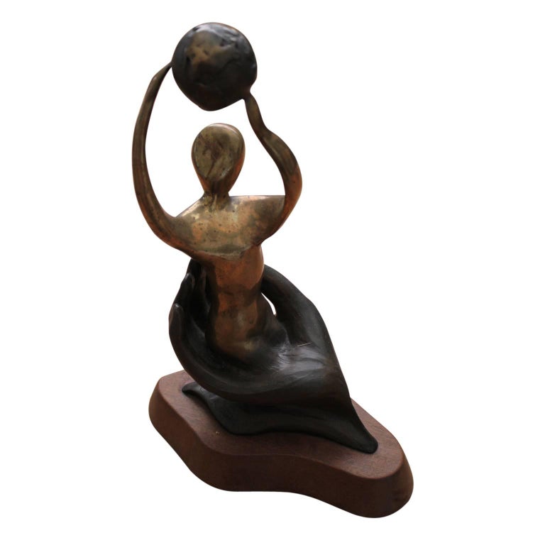 Abstract figurative sculpture of a women holding a globe above her head and is sitting in the palm of a hand. The bronze piece is on top of a wood pedestal. It was given as a Houston Service award in 1986. The artist signed, titled and dated the