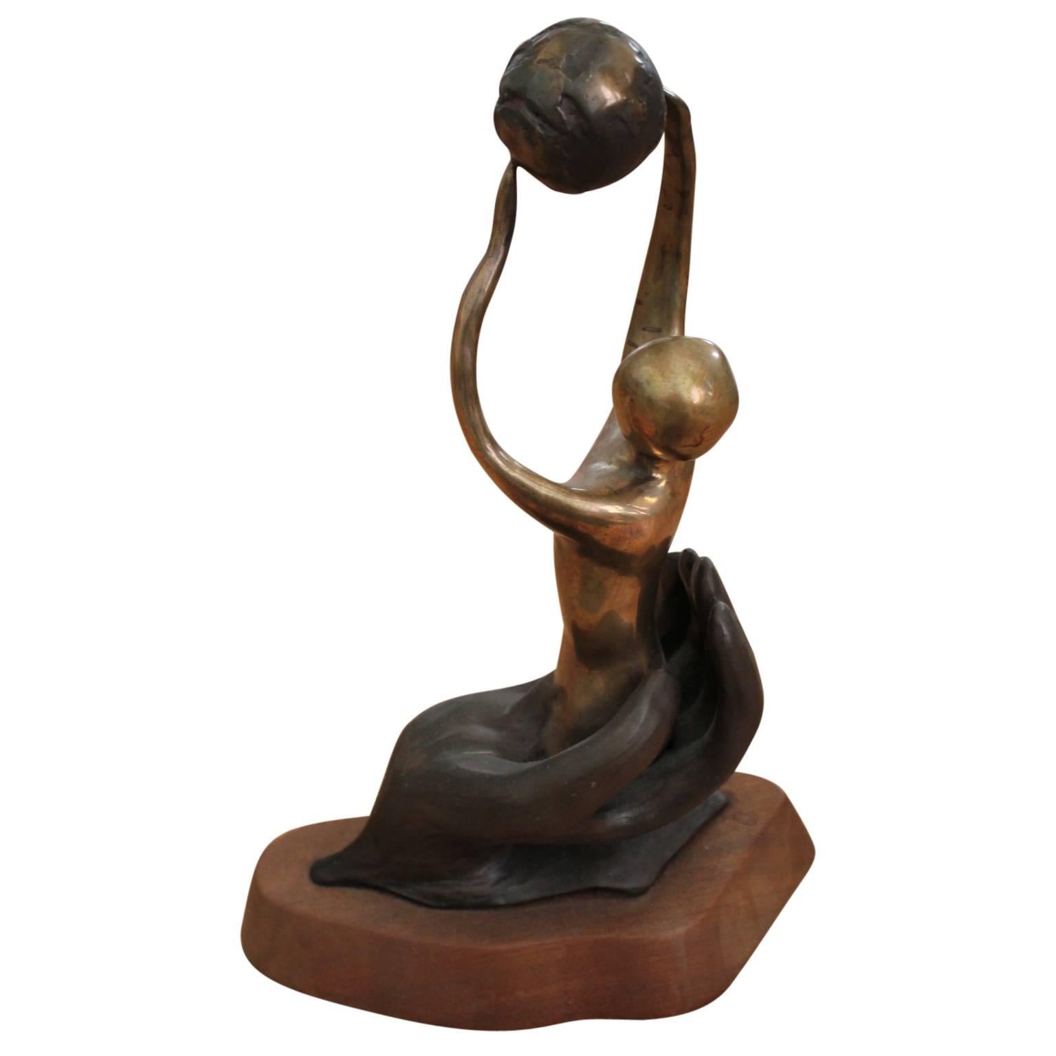 Abstract figurative sculpture of a women holding a globe above her head and is sitting in the palm of a hand. The bronze piece is on top of a wood pedestal. It was given as a Houston Service award in 1986. The artist signed, titled and dated the