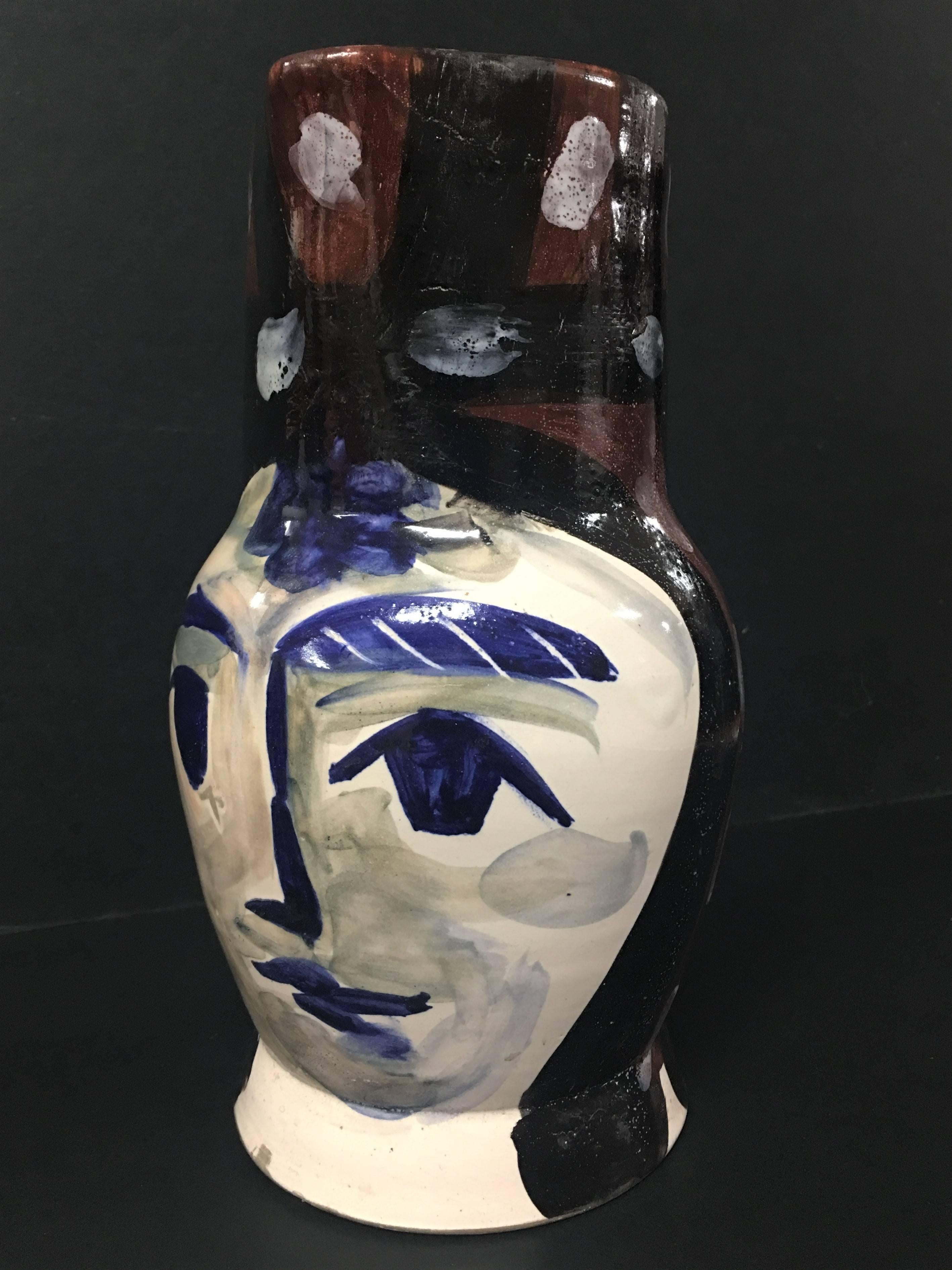This piece is an A.R. turned pitcher created by Pablo Picasso in 1953. It is made with white earthenware clay, decoration in engobes and oxides under partial brushed glaze with white enamel spots in blue, red, white, brown, and black. It bears the