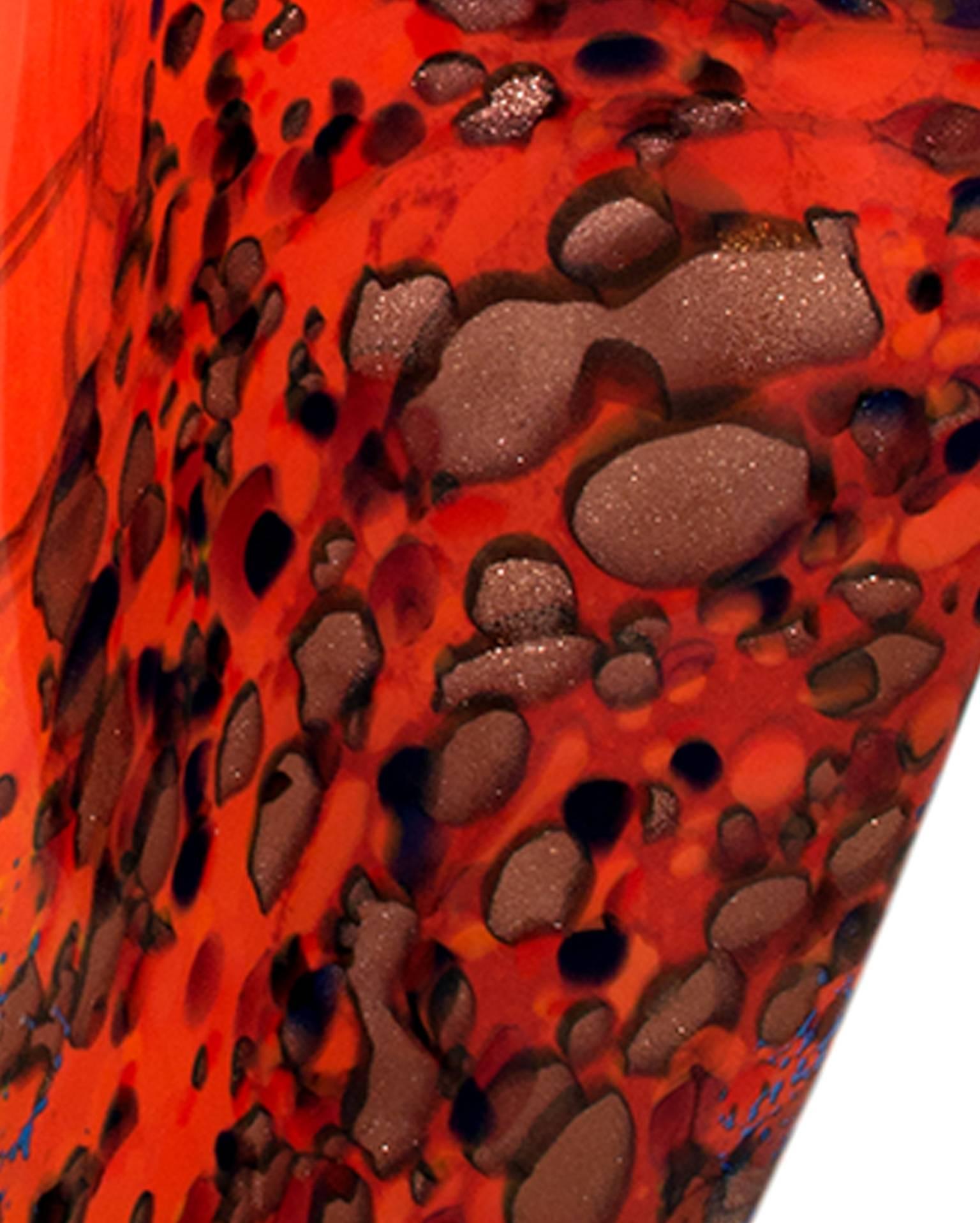 This piece is a hand blown glass vase by Ioan Nemtoi. The artist signed the piece. This vase is wavy and is mostly bright red/orange with various speckled yellow, blue, black, and brown designs. 

13