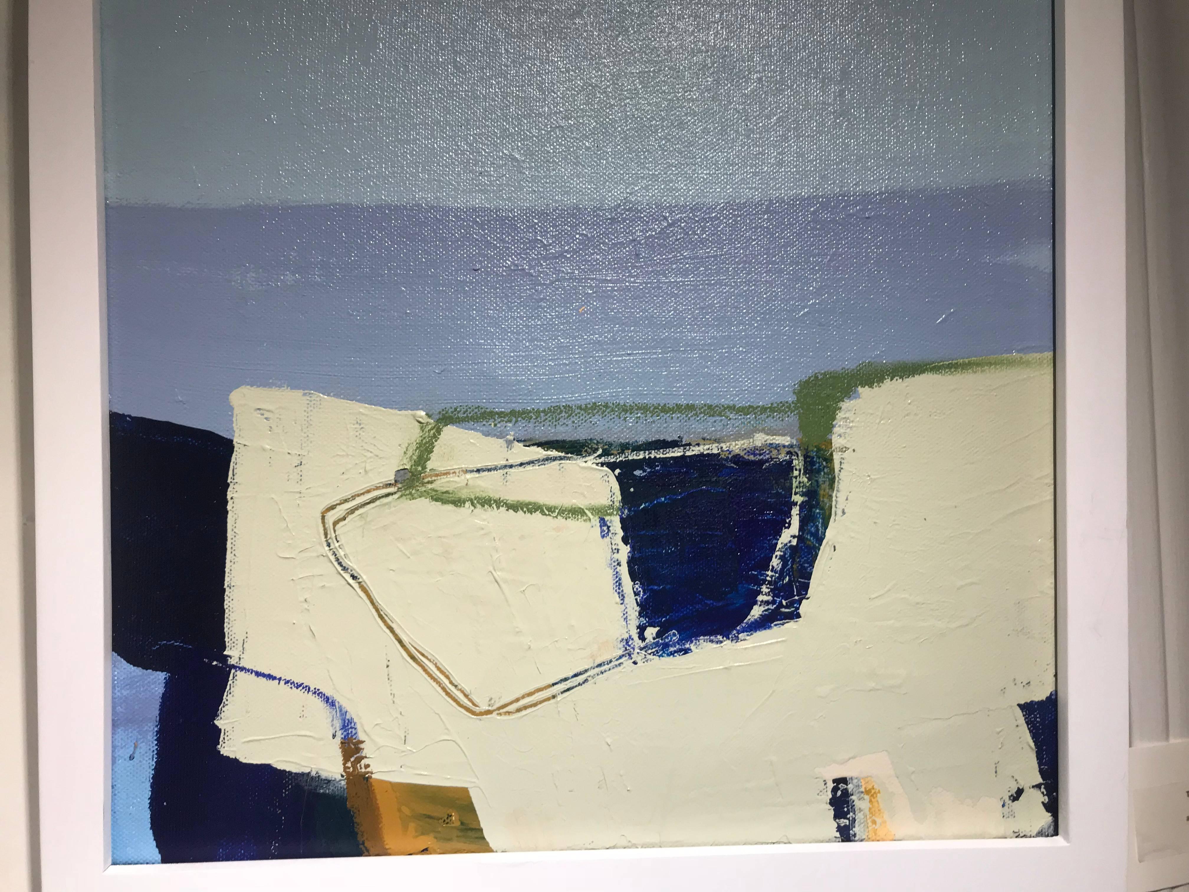 This petite abstract expressionist painting created by American artist Theresa Girard in 2017 is titled 'Shoreline 1'. This framed square shaped painting features a palette made of various tones of blue, beautifully contrasted by slight beige, and