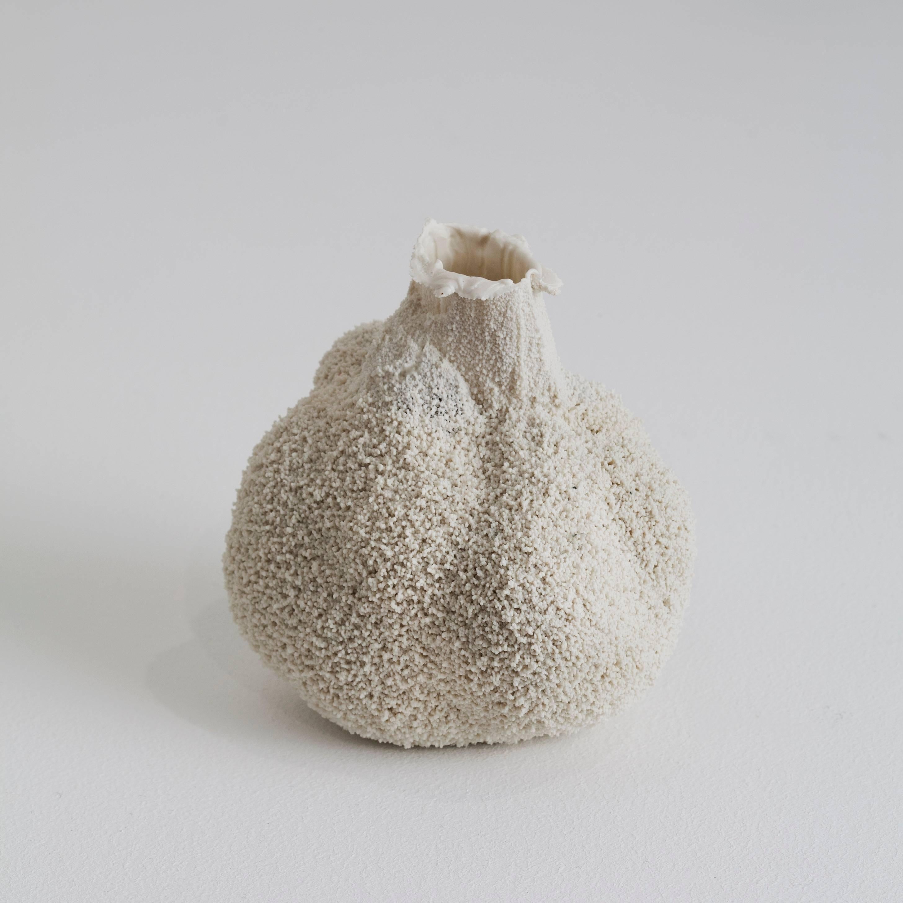 This is a small white ceramic vase by London-based Israeli artist Michal Fargo. She pours liquid porcelain into a hollowed block of foam, allowing it to settle into the pores. The vessel's final shape is determined by the material rather than the