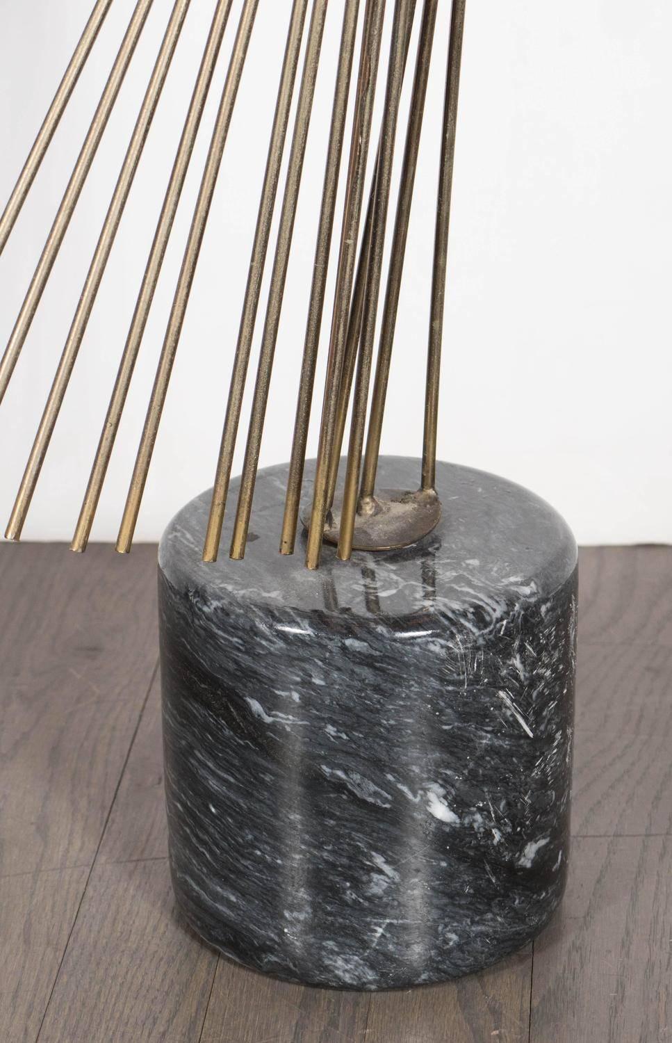 A Brutalist sculpture in patinated brass on a polished black marble plinth by Curtis Jere. It offers a curved fan-like projection of brass rods that meet at a central point. The sculpture attaches to a plinth realized in exotic black belgian marble.
