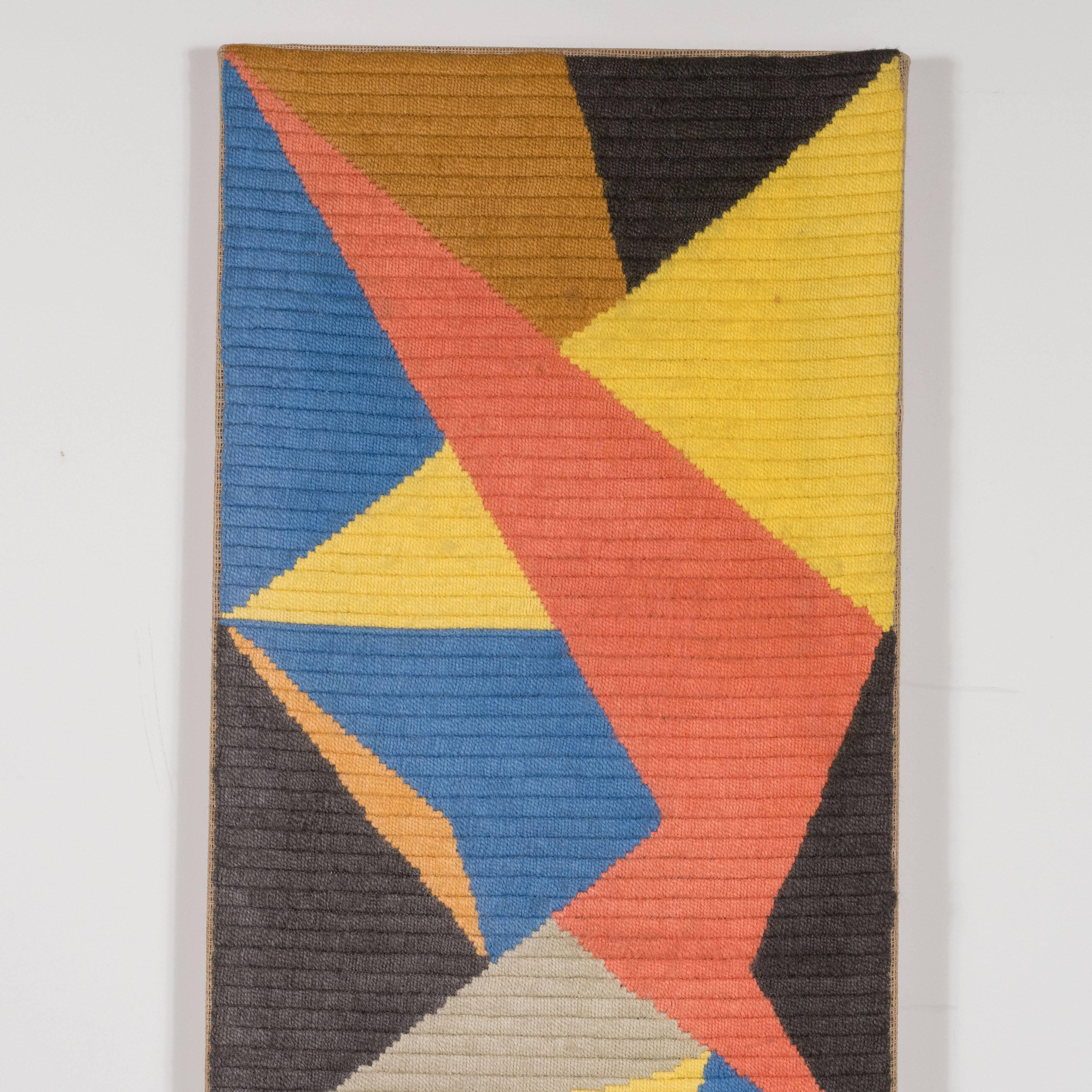 This compelling Mid-Century Modernist tapestry wall hanging was realized in tightly woven, hand-knotted cotton textile. The composition features an array of intersecting planes in a vibrant palate that includes hues of persimmon, hazelnut, lemon