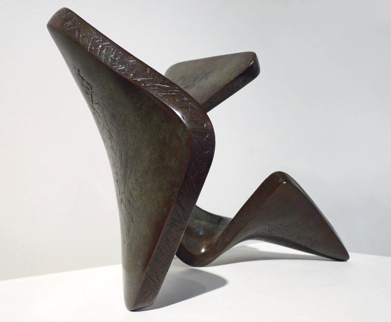 Situ is a pedestal sized, cast bronze sculpture. Edition #2 of 8 (pictured here) has a dark patina in shades of reddish brown and green, and the bronze surfaces are detailed with a crosshatched texture. The work is signed on the back and the edition