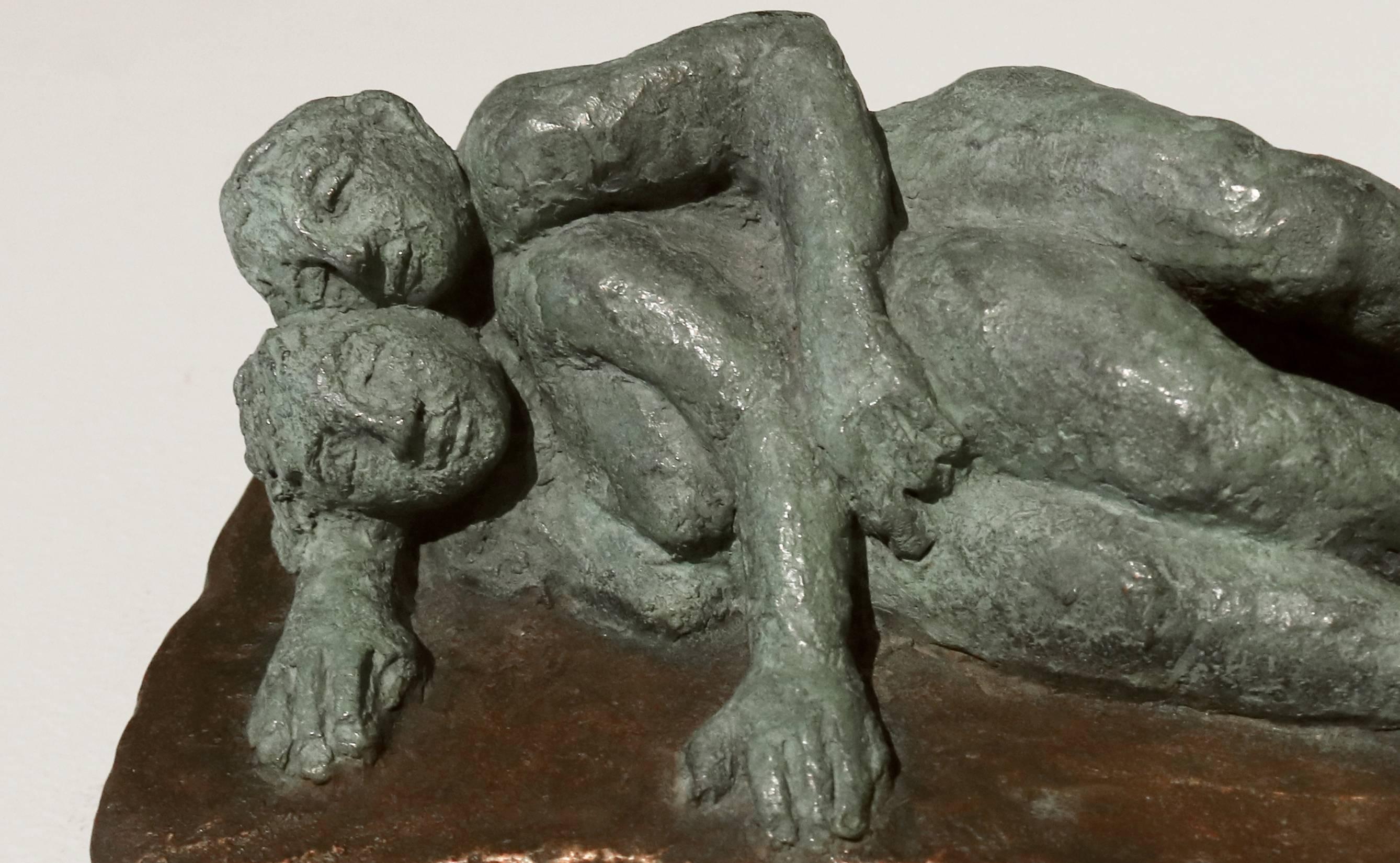This small bronze sculpture features a peacefully reclining couple wrapped in a sweet embrace. The couple are finished with a soft green patina, which contrasts beautifully with the warm bronze surface on which they recline. It is #3 in an edition