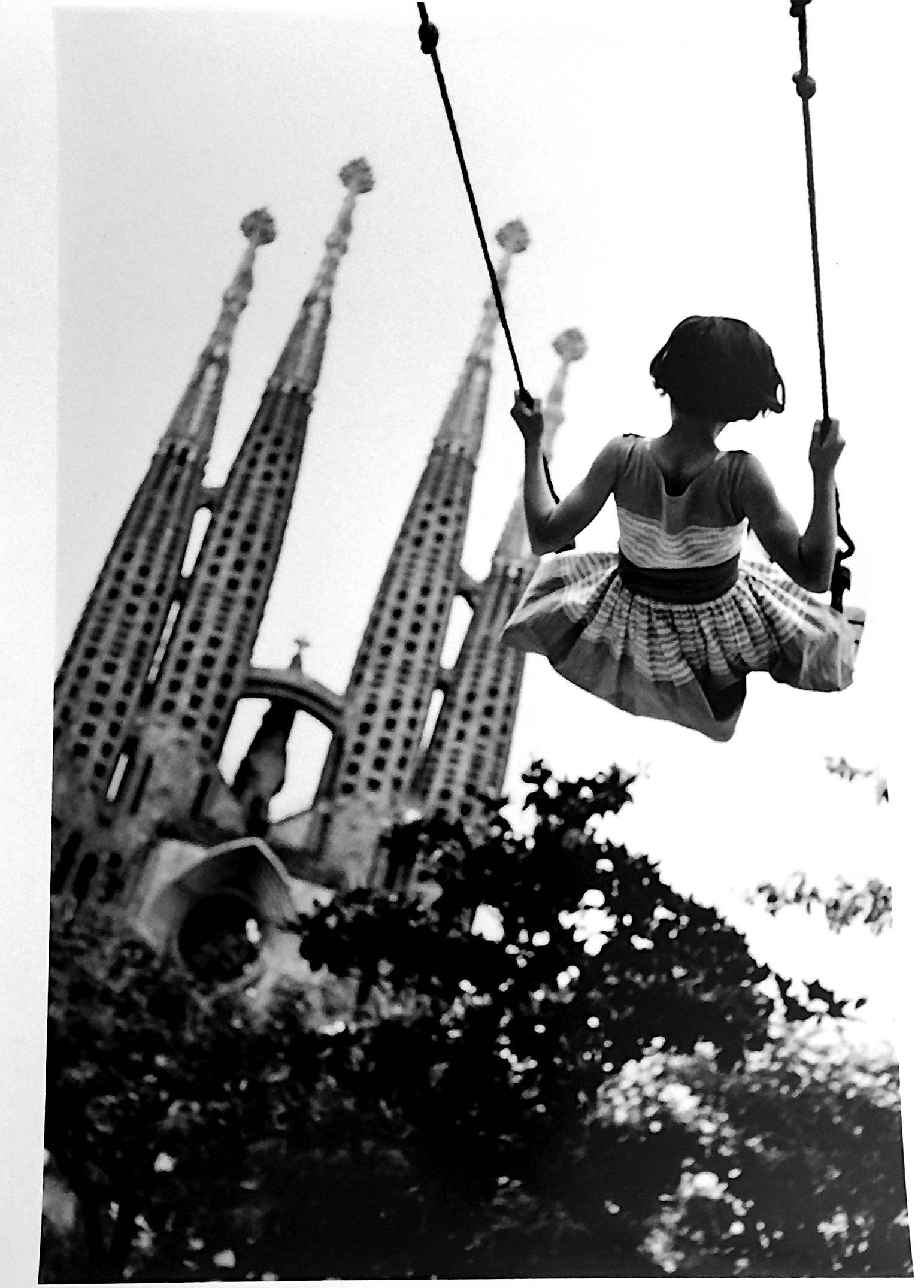 Burt Glinn's The Sagrada Familia, Barcelona, Swing, 1959, is a gelatin silver print, 20 x 16, signed and stamped (authenticated) by the estate. Here, a young girl swings carefree against the backdrop of the architect Antoni Gaudi's magnificent and