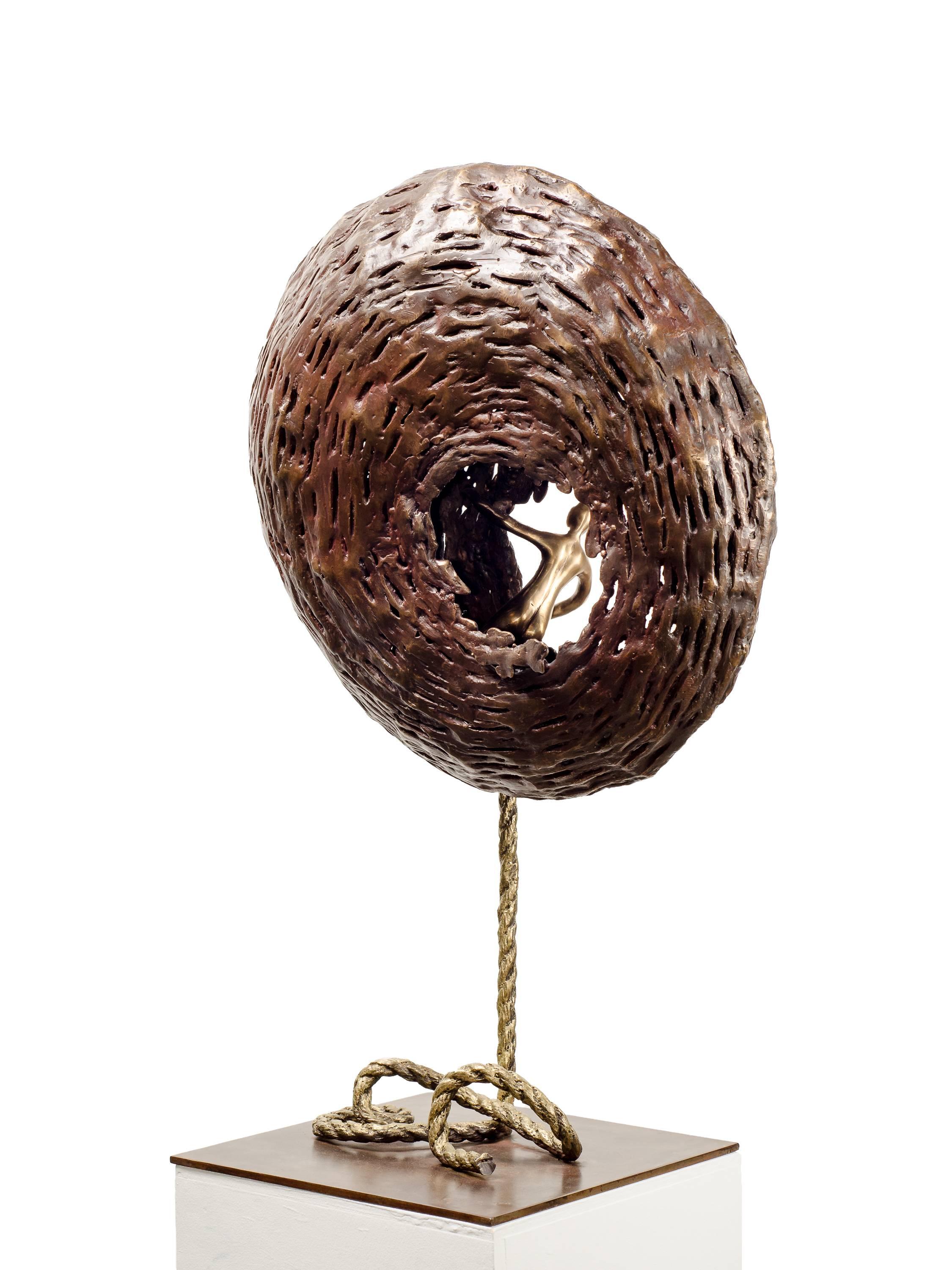 From The Soul is a bronze sculpture by Beatriz Gerenstein where she shows a golden-brown, chrysalis-like structure with and a human figure looking outwards from an opening in the nest. 
The whole sculpture seems to be floating. It is light and heavy