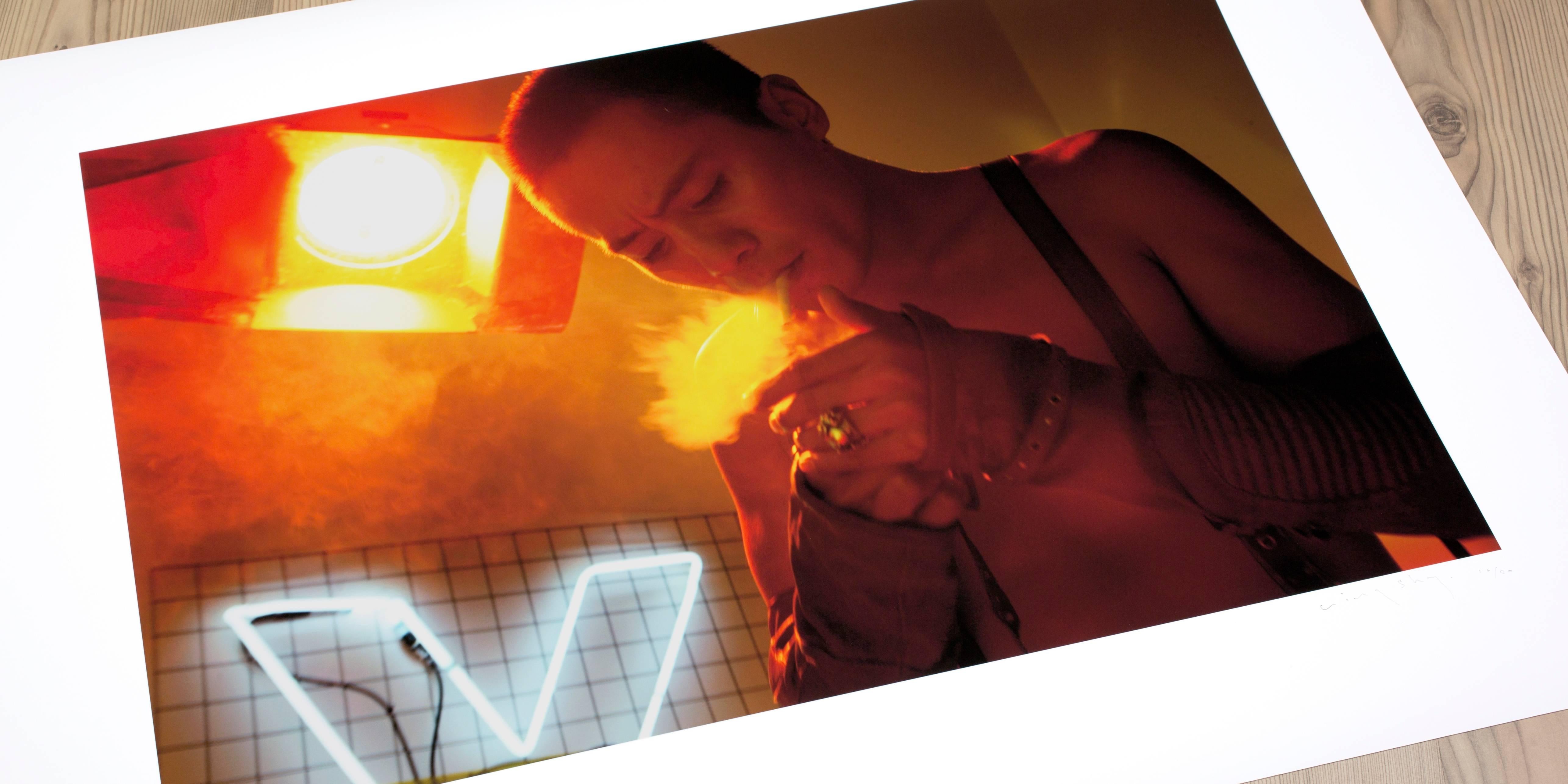 Life on fire. All shades of red and orange in this electric fashion editorial photo of the subject determinedly arranging a cigarette in a neon-lit space. 