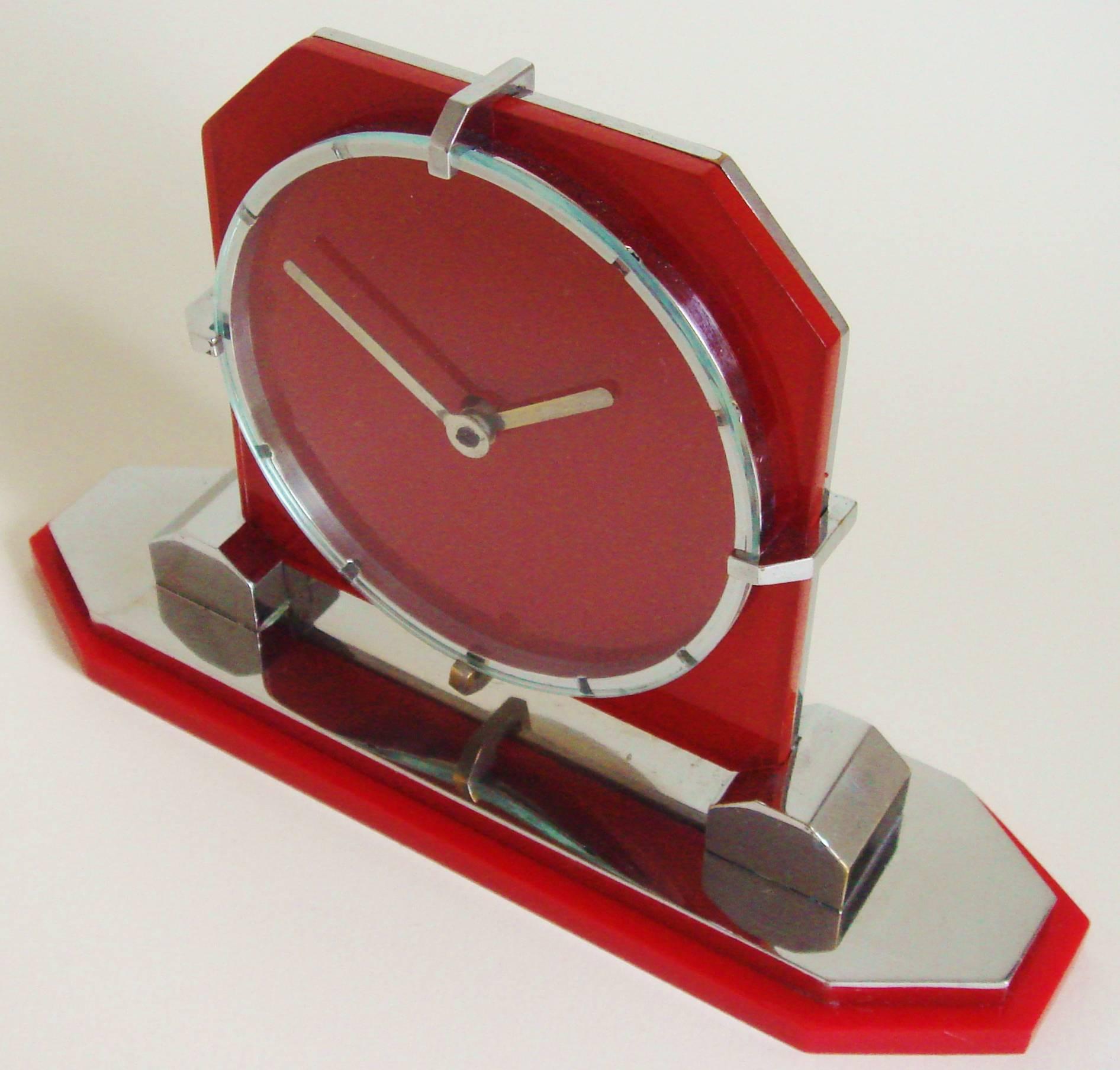 This exquisite pre-war English Art Deco chrome desk clock features a red glass face-plate backed with chrome that is mounted to a red Lucite base and is stamped to the obverse with an English patent number for 1932. This particular example was