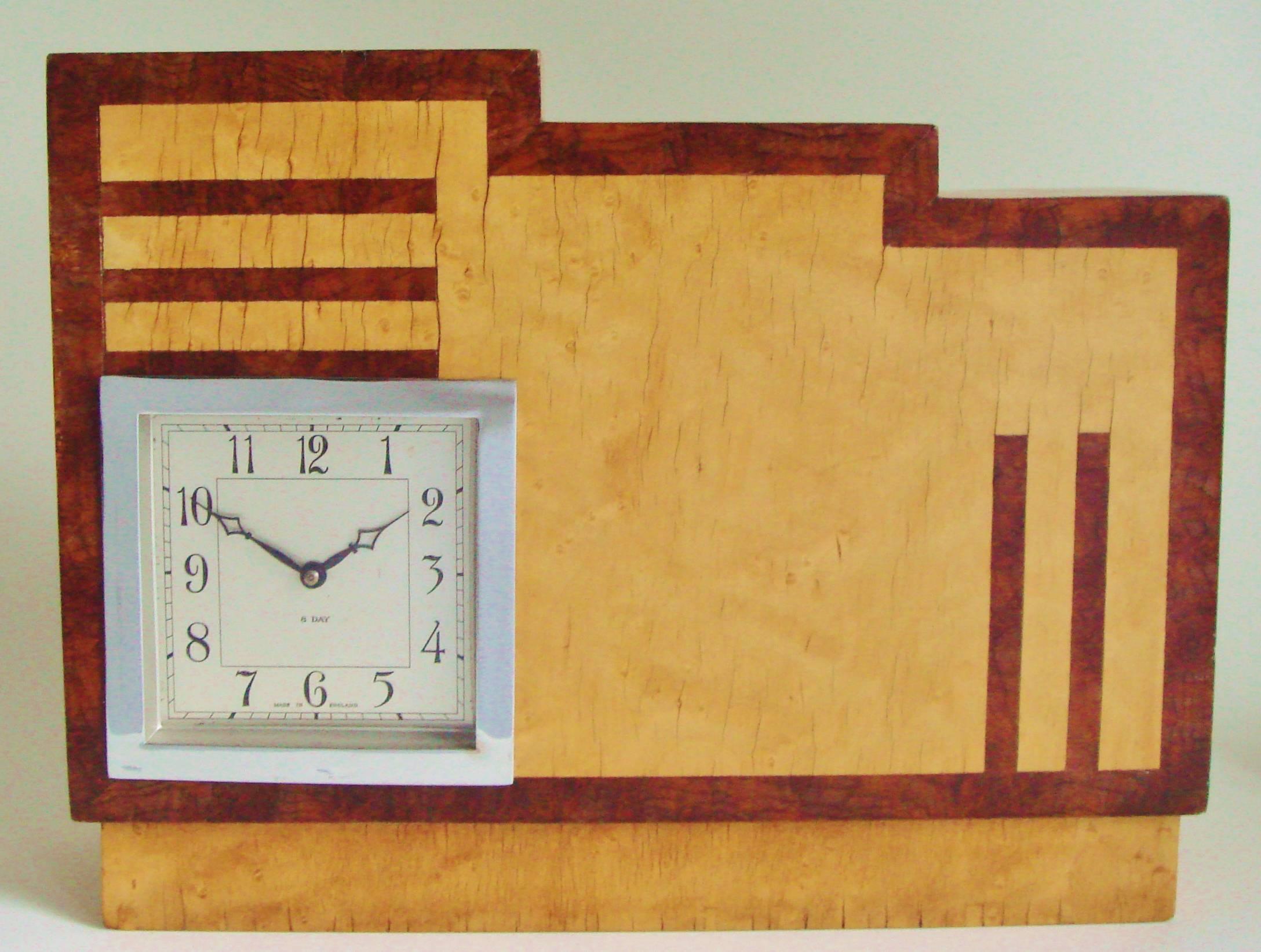 This extremely architectural English Art Deco mechanical mantle clock features a geometric inlaid veneered pattern of blonde birds-eye maple contrasted with burl walnut. The body of the clock is cut from a laminated block of wood that is