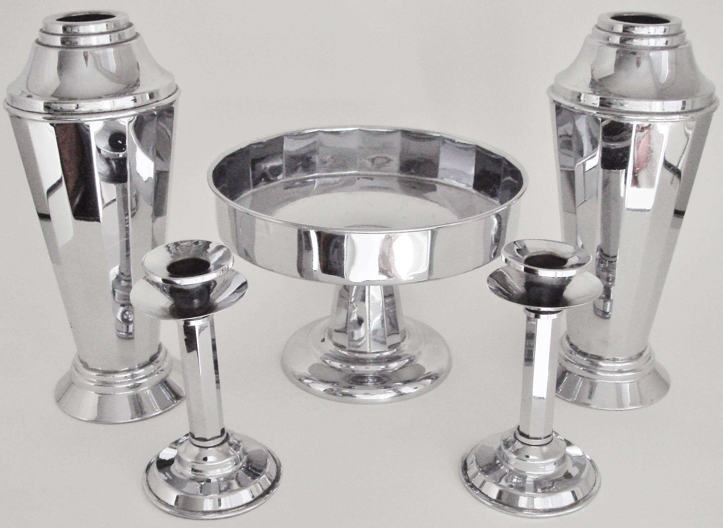 This 5-piece English cocktail shaker vases, candlesticks and pedestal fruit compote console set is by Beldray (Bradley and Company of Bilston, Staffordshire) who began producing metal ware in the Arts and Crafts style in 1903. The company had a