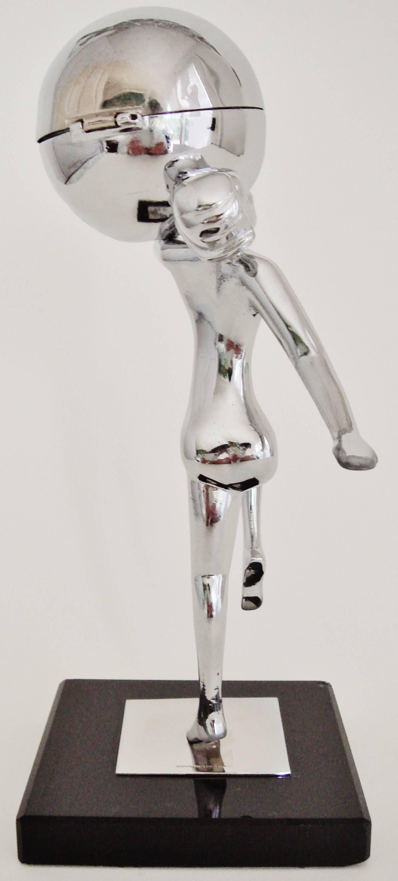 This English Art Deco chrome plated stylized nude holds a ball containing a wheel and flint lighter and marches on a chrome square fixed to a base of bevelled black Vitrolite. The nude is clearly fashioned after the Hagenauer figures of the period