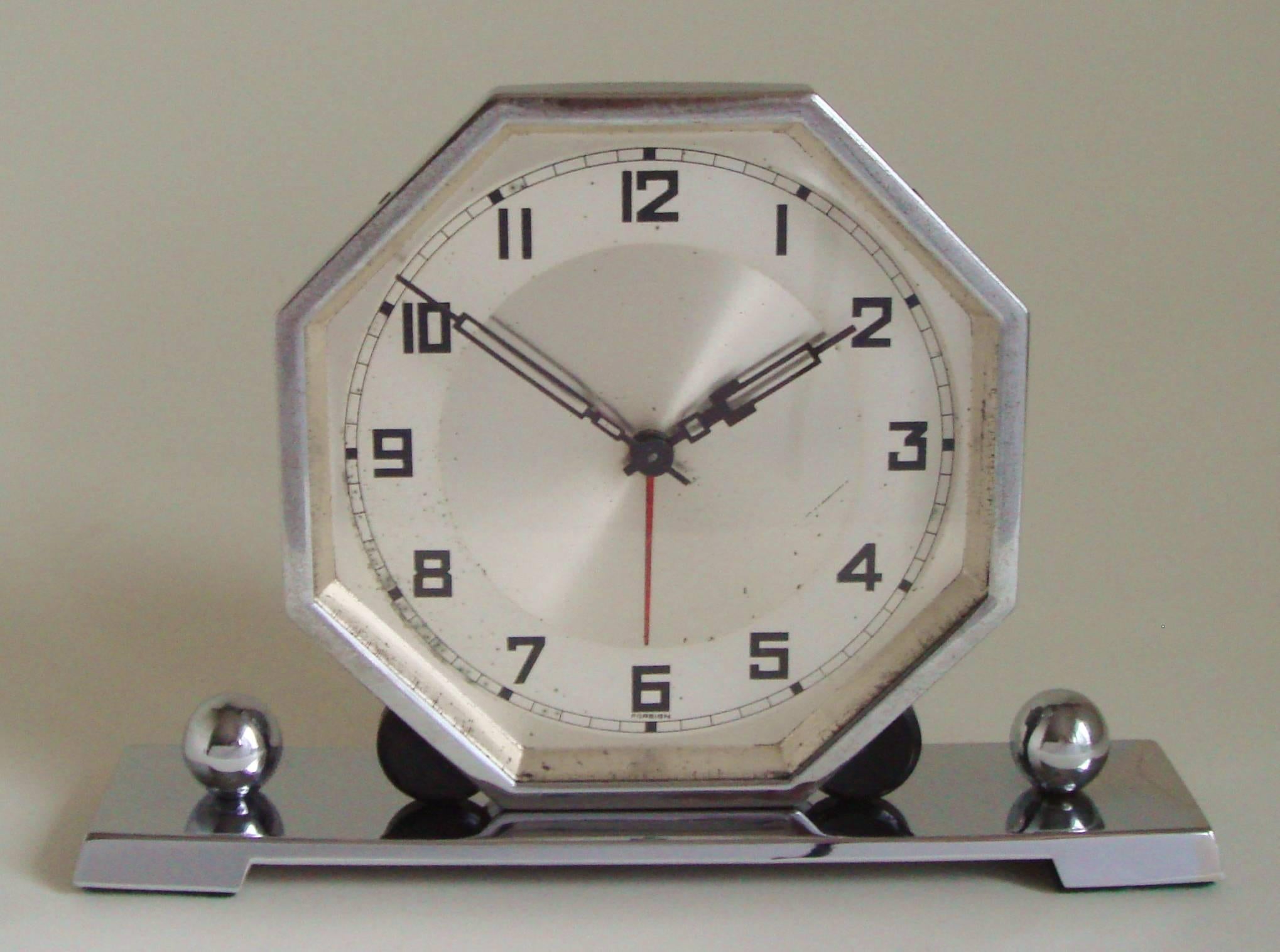 The hexagonal chrome body and bezel of this German Art Deco alarm clock stands on an oblong chrome footed plinth and is held in place by two demi-lunes of black Bakelite and bookended by two chrome spheres. The face does have some age spots but the