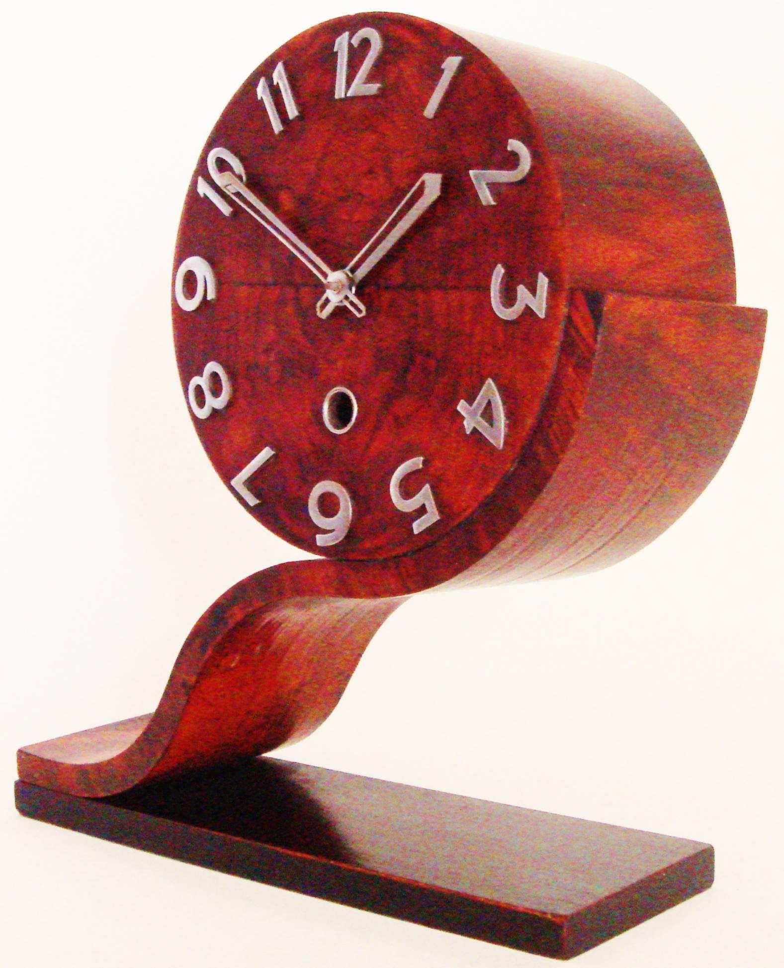 This iconic English Norland Art Deco mechanical asymmetrical mantle clock is a triumph of the design of the inter war period. A tilde or wave shaped walnut support rises up from an oblong ebonised base and is topped with a drum shaped clock case