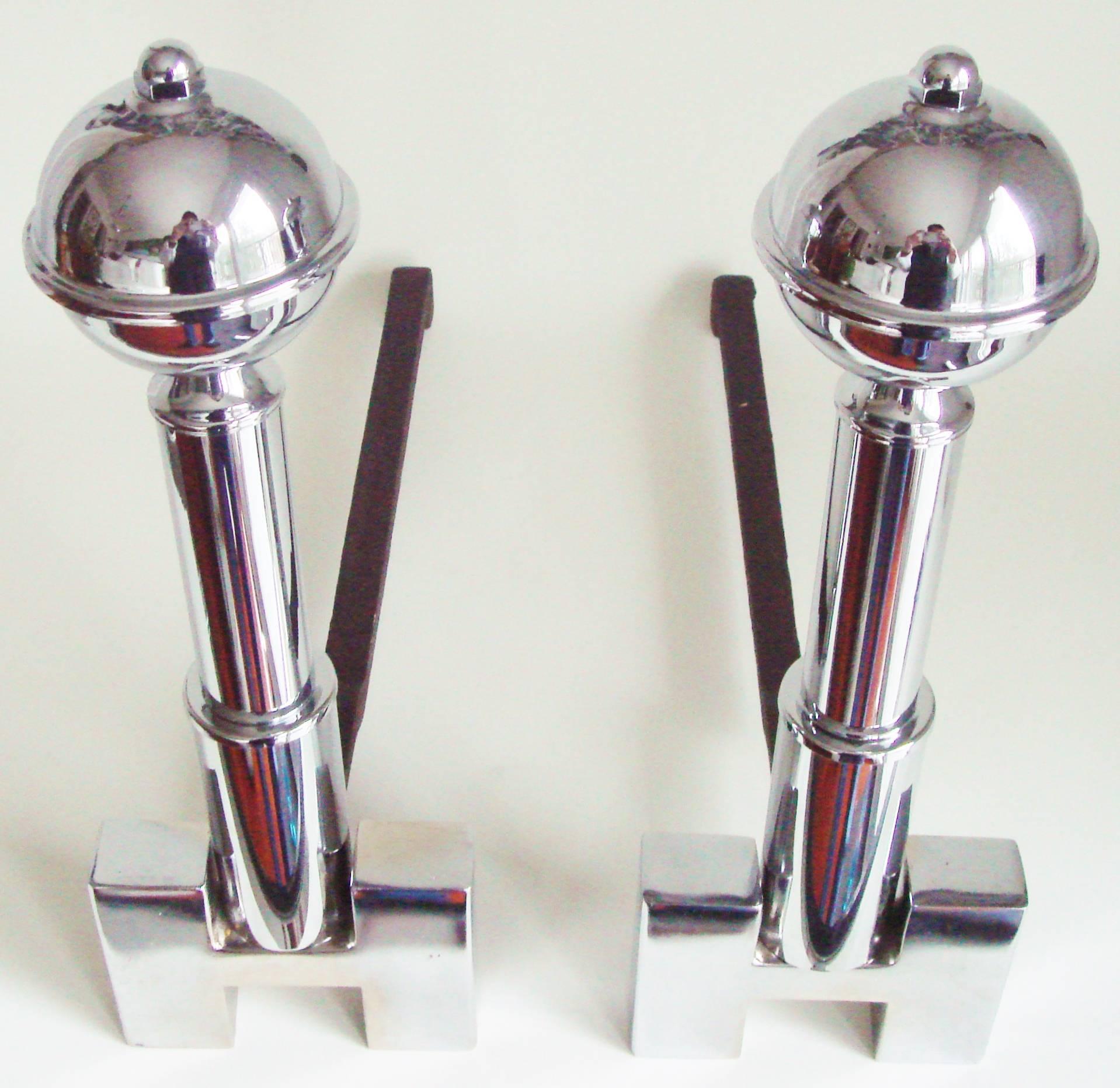 This beautiful pair of American Art Deco chrome-plated geometric andirons each feature planet style orbs that top a skyscraper shaped two stage pillar that rises from the crossbar of an 'H' shaped plinth. The chrome is in excellent condition as are