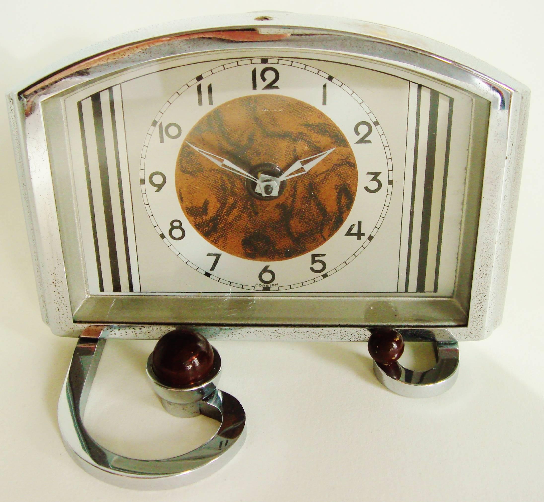 This eccentrically designed German chrome-plated table clock features a typically Art Deco styled face with vertical black bands either side of a faux grained circle to emphasize its silver geometric hands surrounded by 