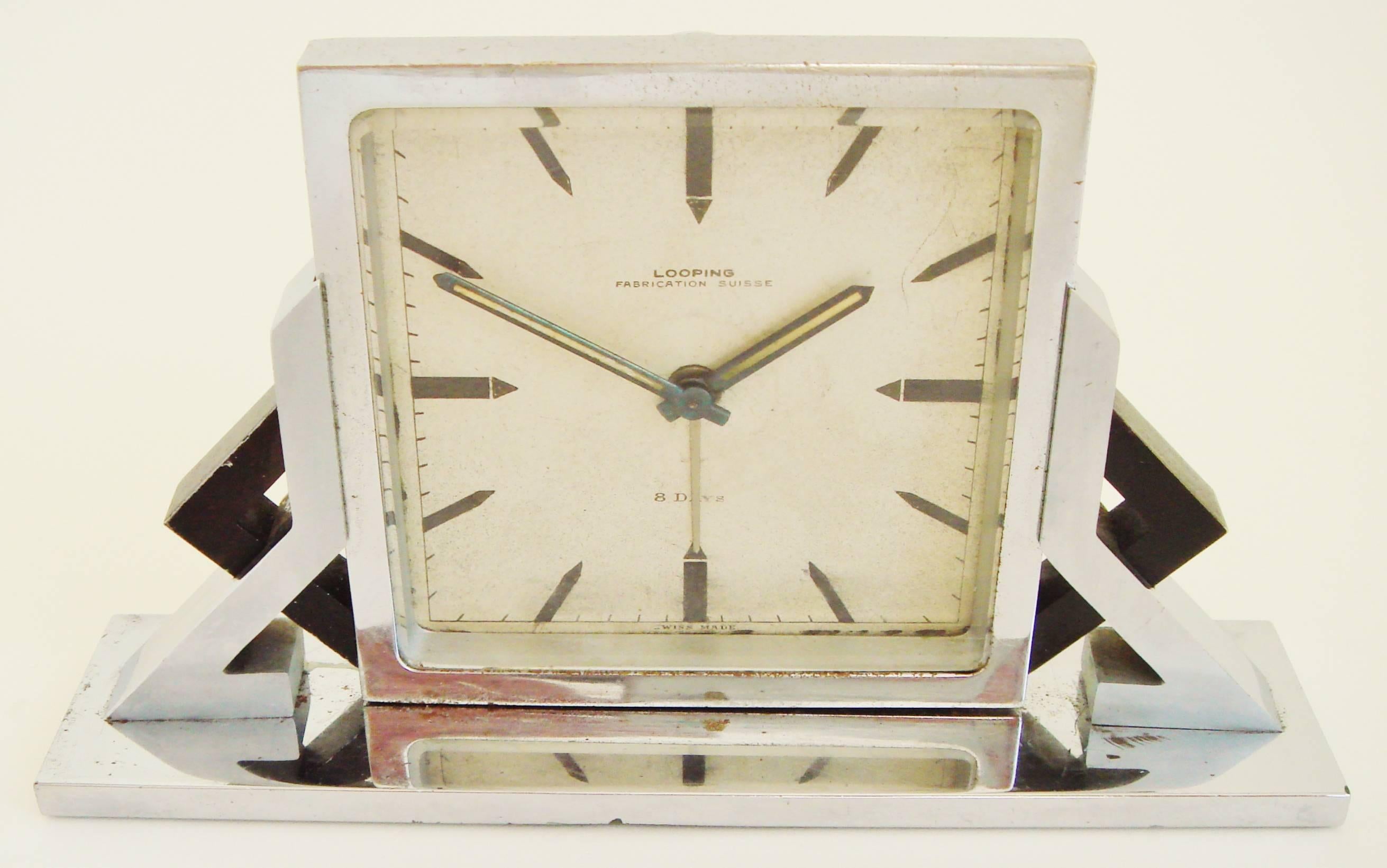 This very stylish geometric Swiss Art Deco 8-day alarm clock juxtaposes jagged shapes in polished chrome, brushed chrome and matte black enamel on either side of the polished chrome bezel. The numerals are represented by black oblongs capped by