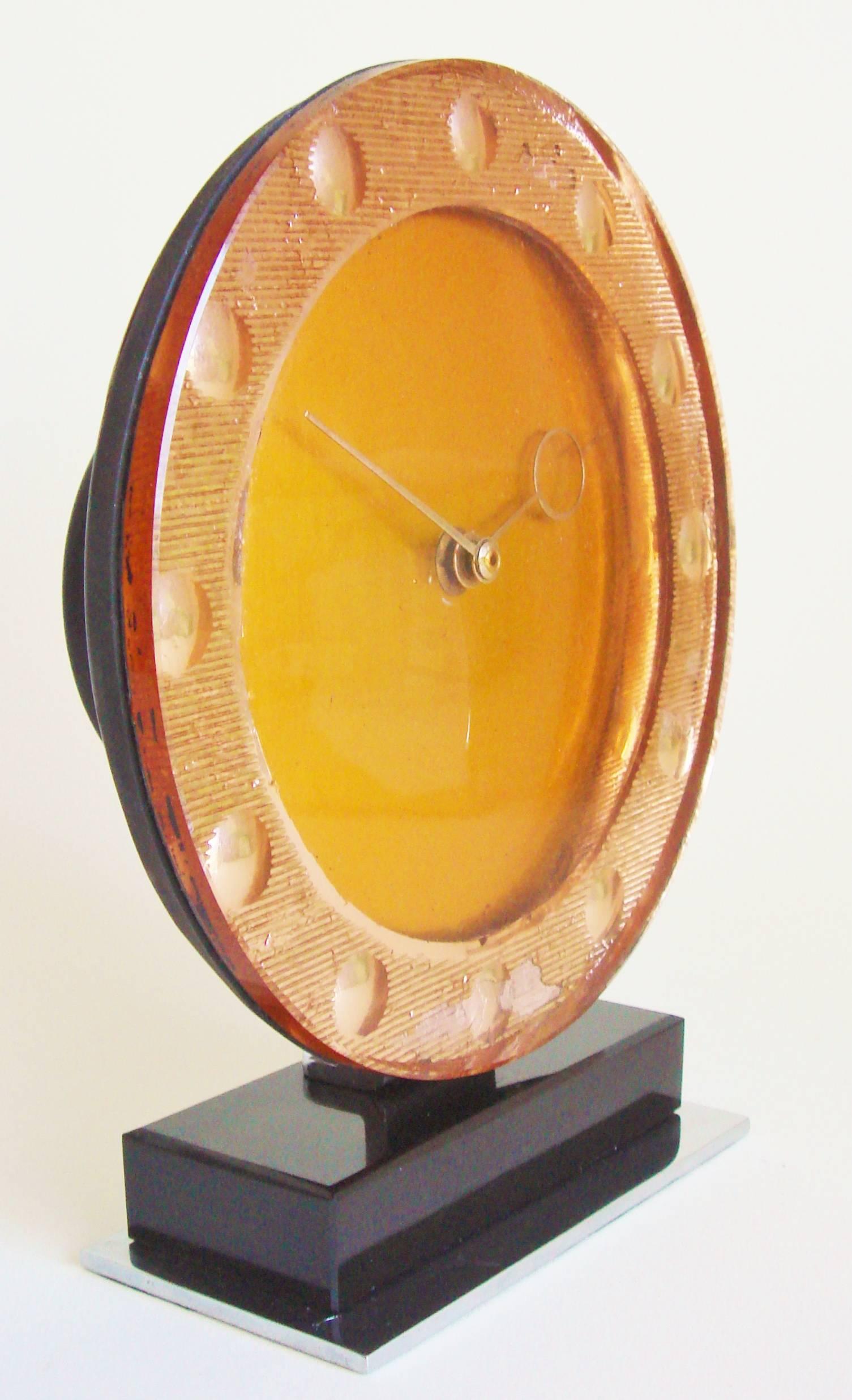 This stunning English Art Deco table clock features a thick glass face covering a silvered peach foiled bezel with reverse-cut dome numerals. The very Art Deco styled brass hands would seem to identify the unsigned clock as having been made by