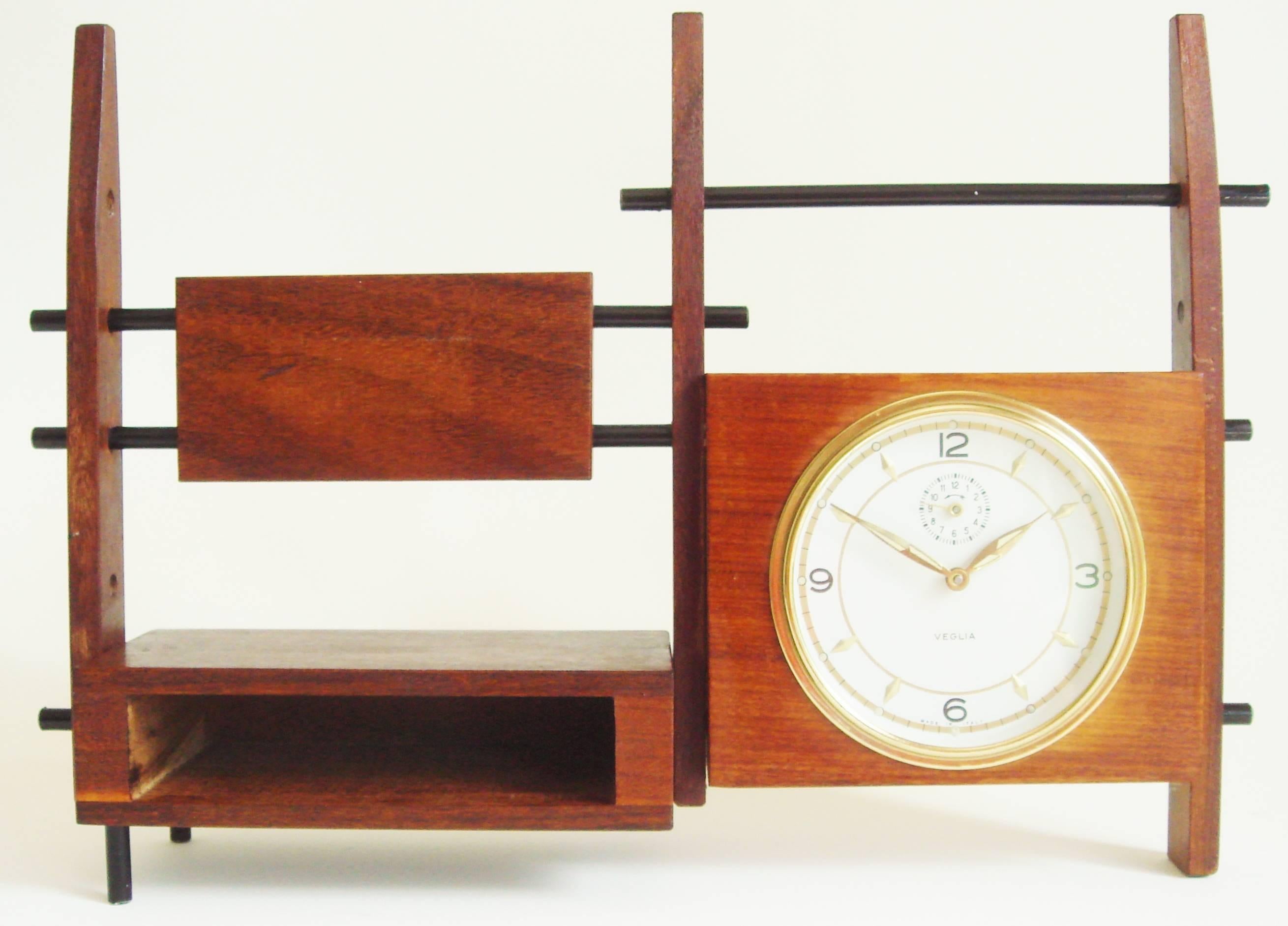 This beautifully executed Italian Mid-Century Modern Veglia mechanical alarm clock takes the form of a miniature wall unit and its design plays off the contrasting surfaces of teak and rosewood. Three tapering vertical posts support a rosewood