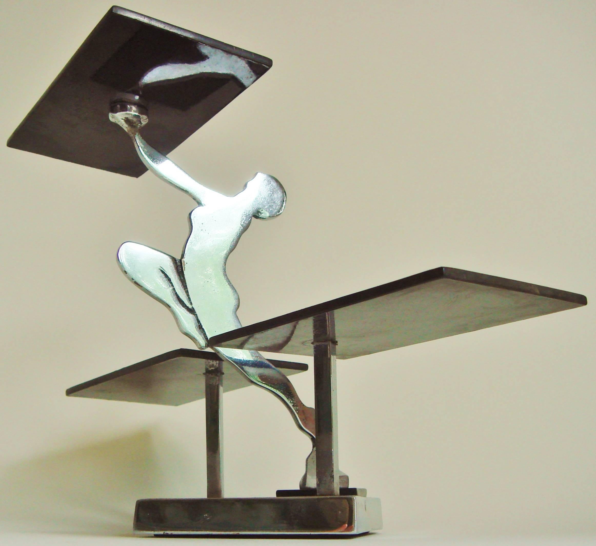 This distinctive and rare piece features a silhouetted female nude holding aloft a black bakelite tray. She stands on one leg and launches herself from a stepped chrome base that rests on a black Bakelite square mounted to a three inch square thick