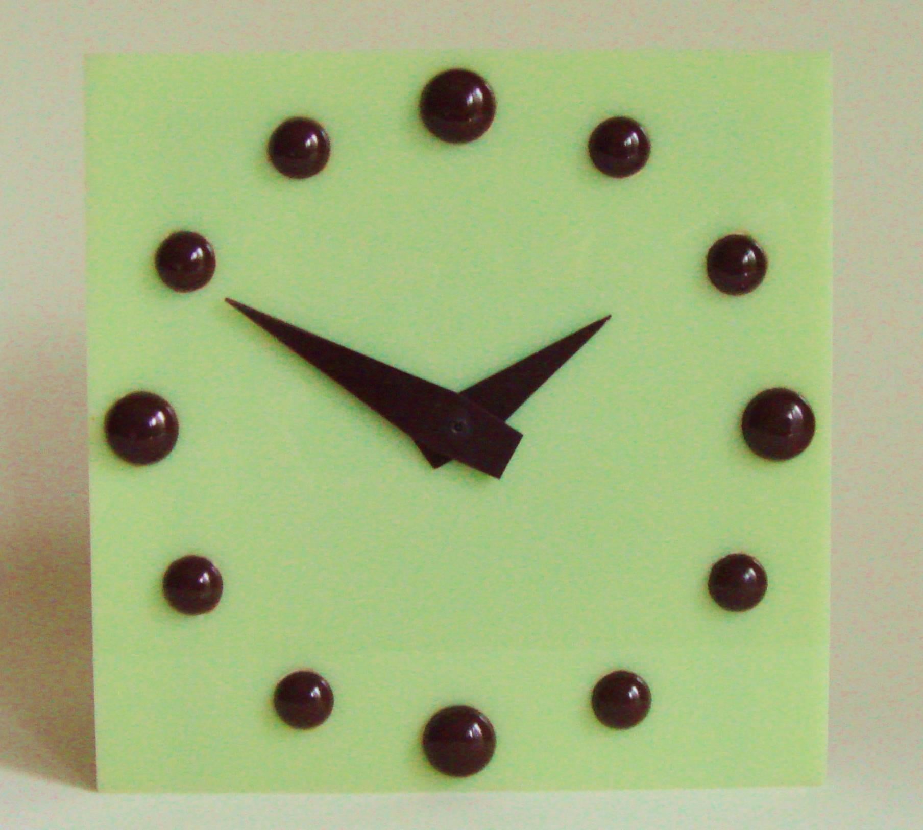 This beautiful and stylishly designed English pistachio Lucite and brown Bakelite electric table clock is stunning in its simplicity. The clock face is a square of solid pistachio Lucite, the numerals are represented by 12 hemispheres of rich