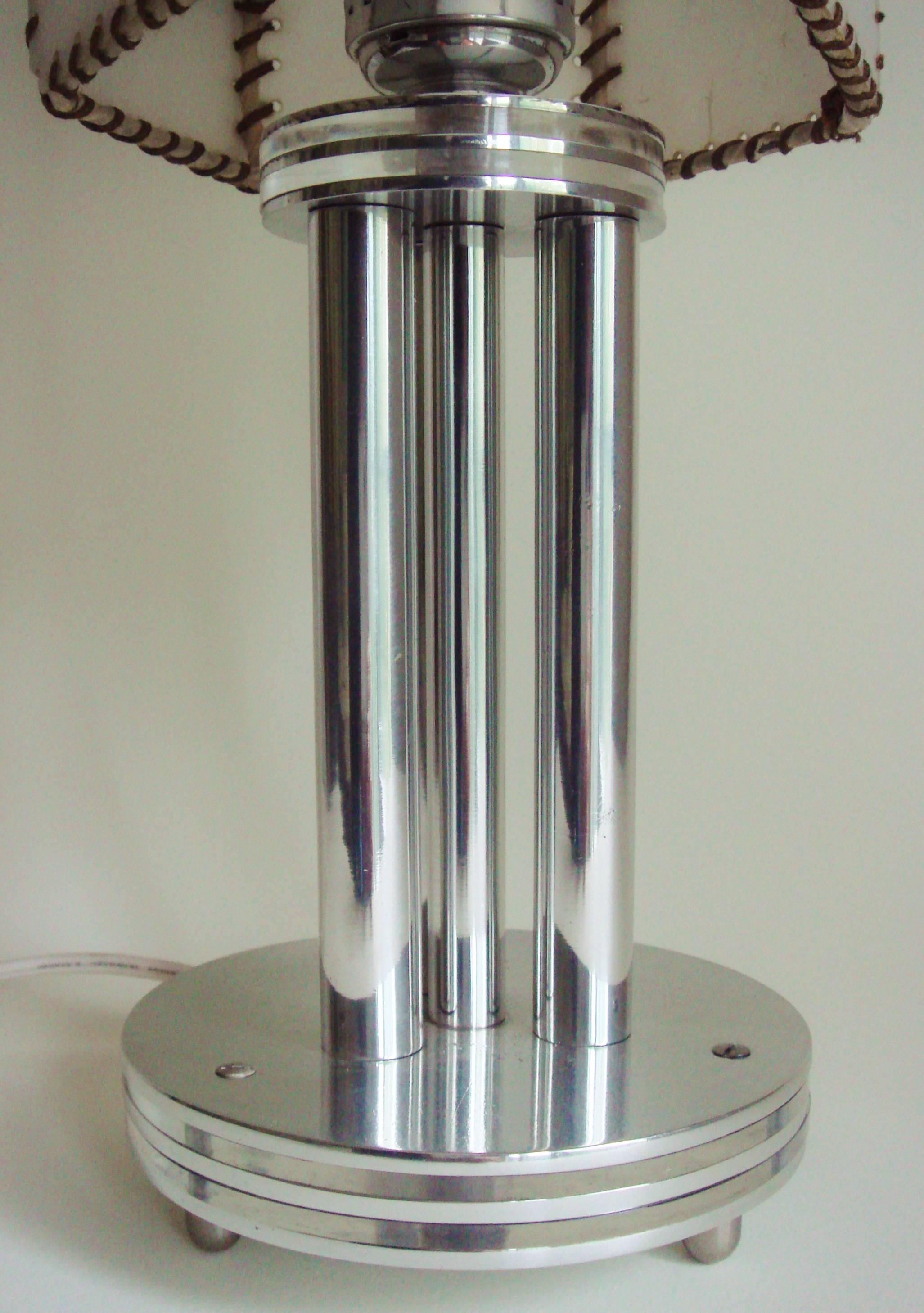 This American Art Deco/Machine Age table lamp features a circular disk base composed of two layers of clear Lucite sandwiched between three layers of polished aluminum and stands on three rounded brushed aluminum feet. Rising up from this base is a