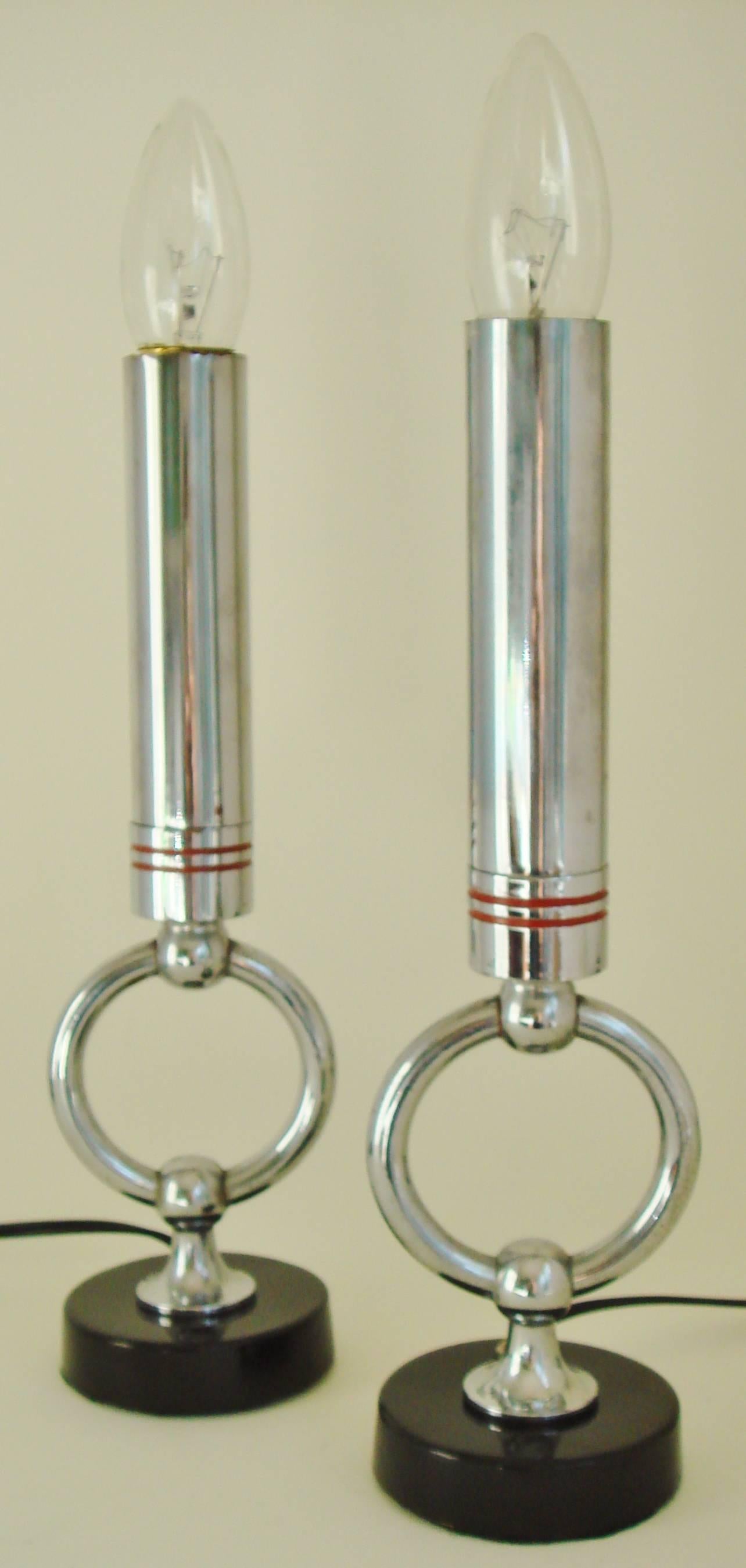 This rare and stylish pair of American Art Deco electric candlestick lamps each feature a polished chrome tube as the body of the candle resting on a socket base that is banded with two incised red enamel rings. This is mounted to a vertically