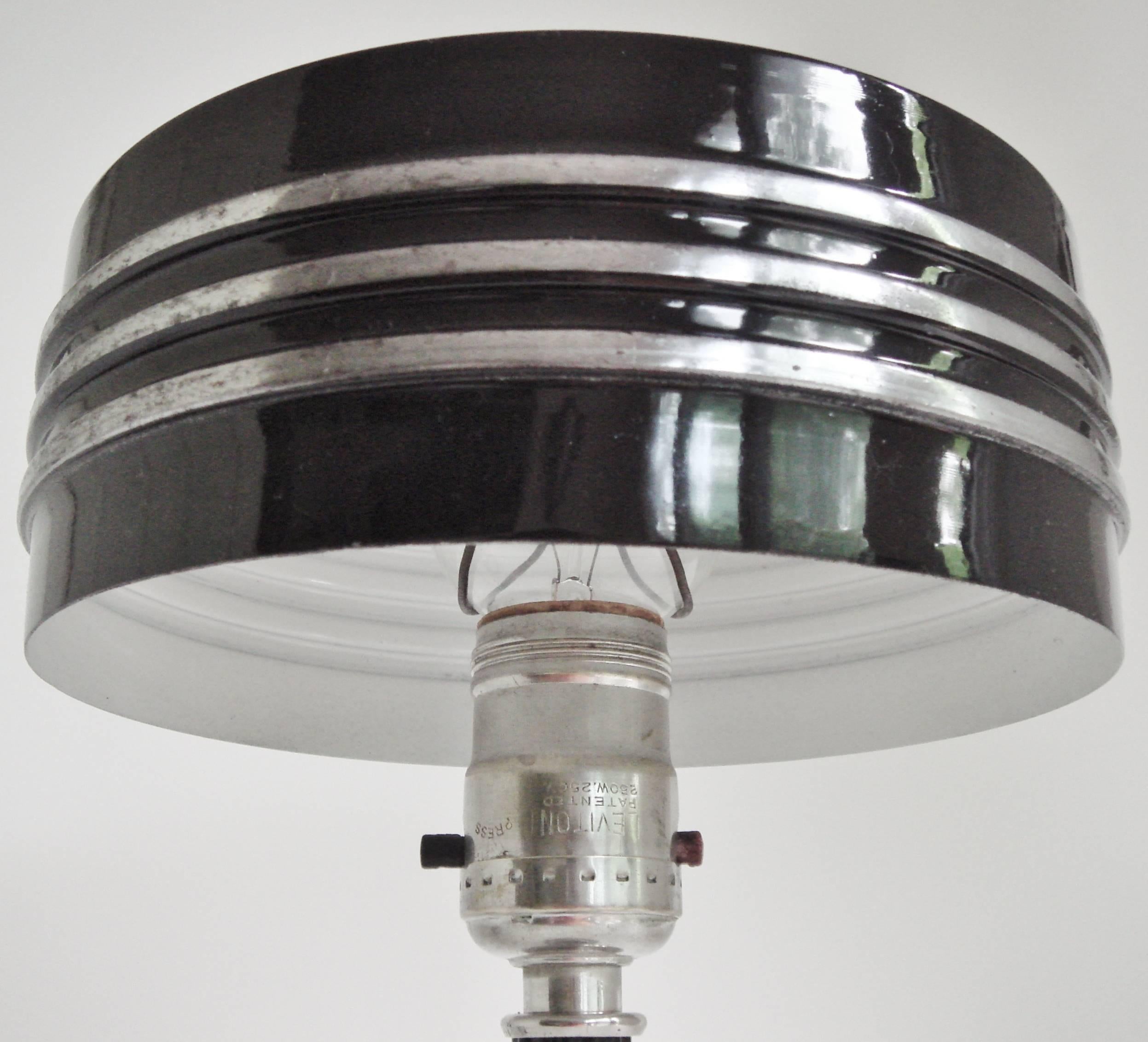 This rare American Art Deco chrome and black enamel table lamp is by the Markel Corporation of Buffalo, New York. It bears their distinctive signature chrome finial to the top of its triple banded drum shade. It has a stepped fluted shaft with
