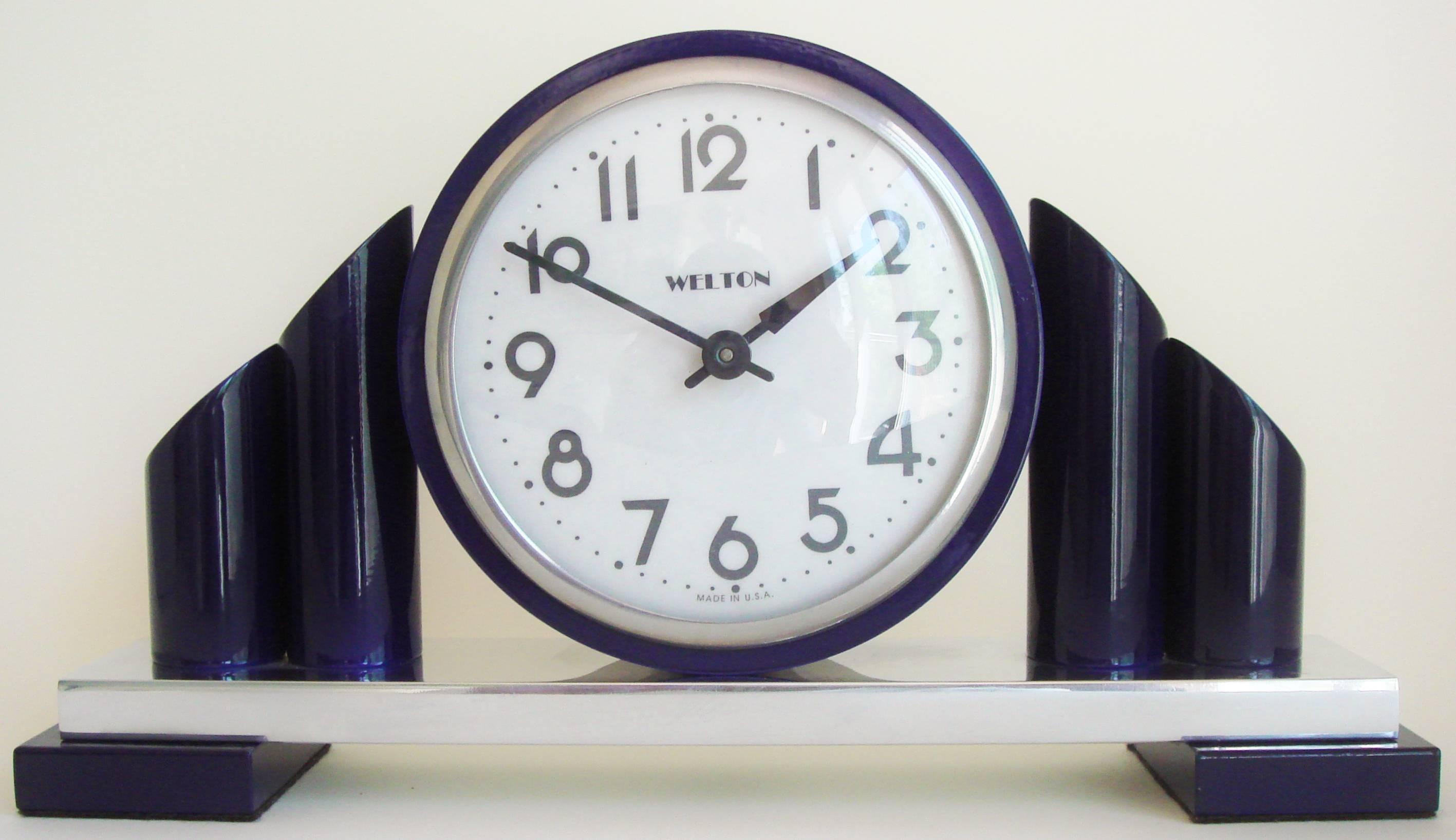 This very stylish American Art Deco Revival mechanical mantel clock features a body in high gloss, metallic and royal blue enamel with chrome accents that houses a traditional brass 8-day movement. Both the numerals and the Welton name are in Art