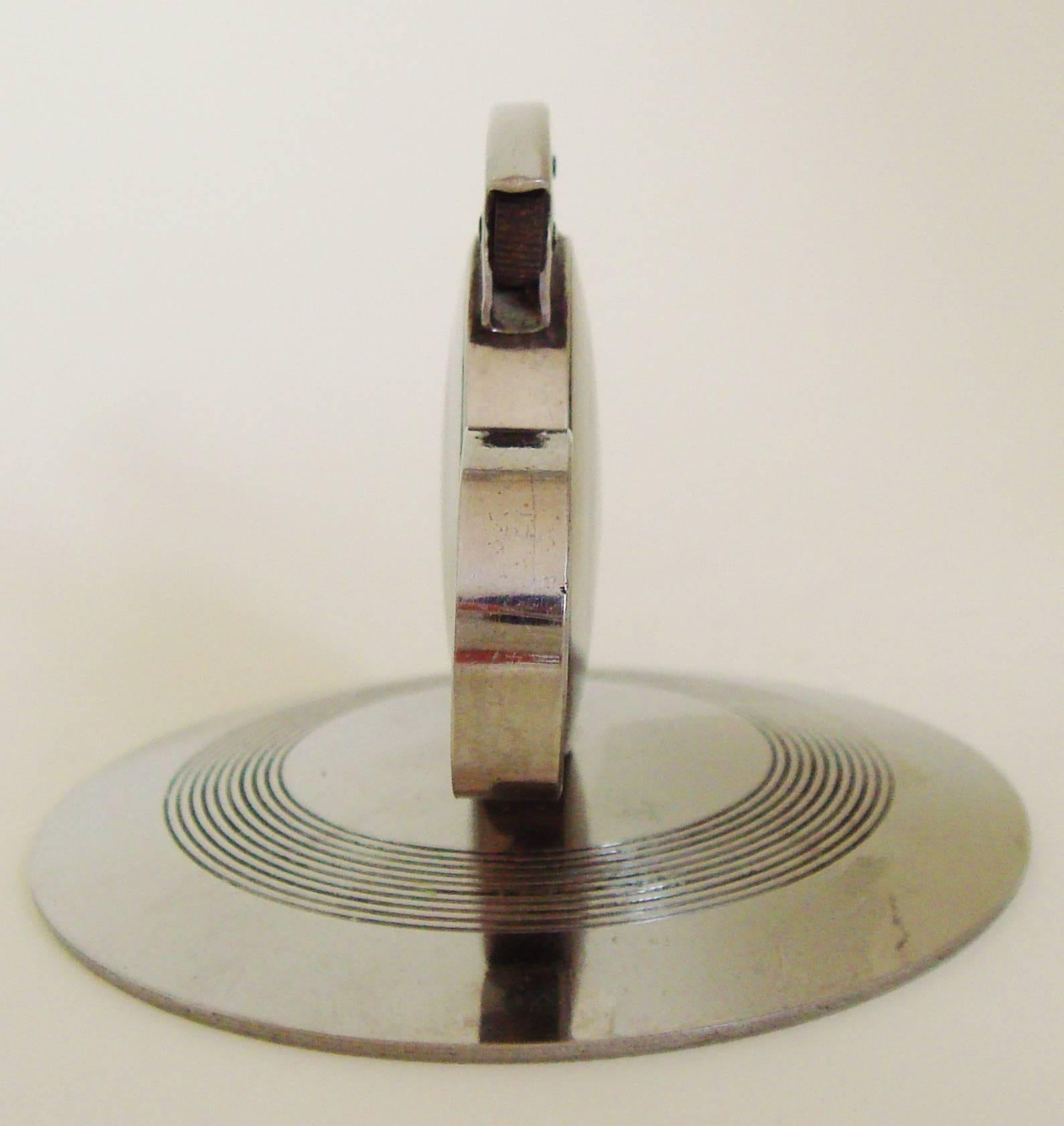 This very stylishly designed small Japanese Art Deco chrome mechanical wheel and flint table lighter is designed like a chamber-stick. It has a finger ring to pass the lighter round, a hinged cap to cover the wick and incised rings for decoration on