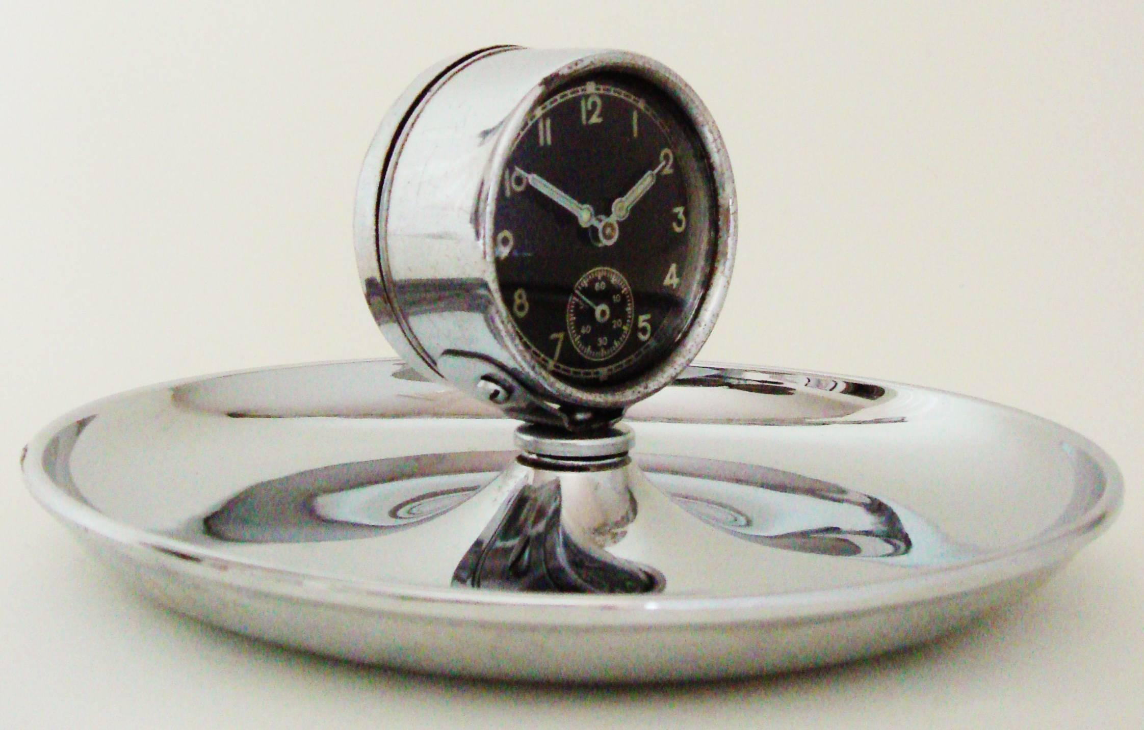 This unusual German Art Deco chrome cigar ashtray features a circular chrome dish with a black-faced 2.13 in diameter mechanical clock mounted to the center. This piece displays beautifully with the dish in excellent condition and the clock itself
