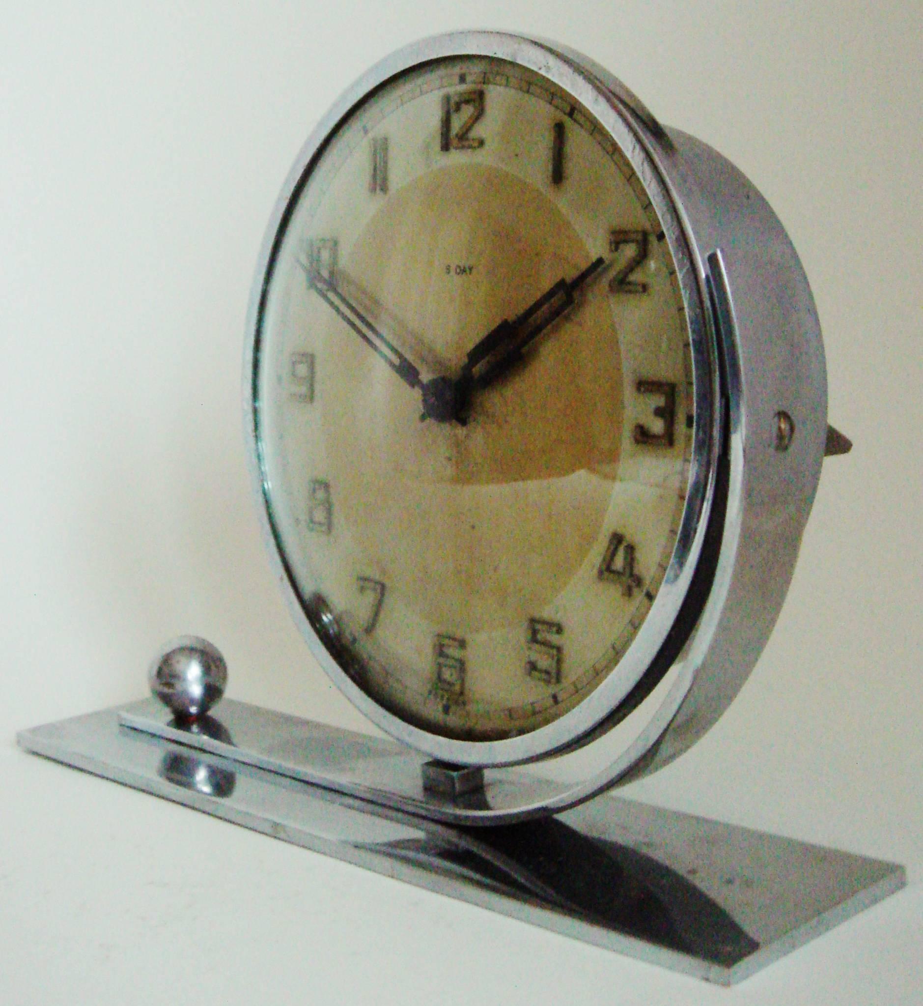 This stylish German Art Deco asymmetrical, 8-day, mechanical desk clock features a circular face with a chrome bezel mounted to a curved chrome strip. This is anchored to an oblong chrome base by a chrome sphere. The face is stamped 8 Days and