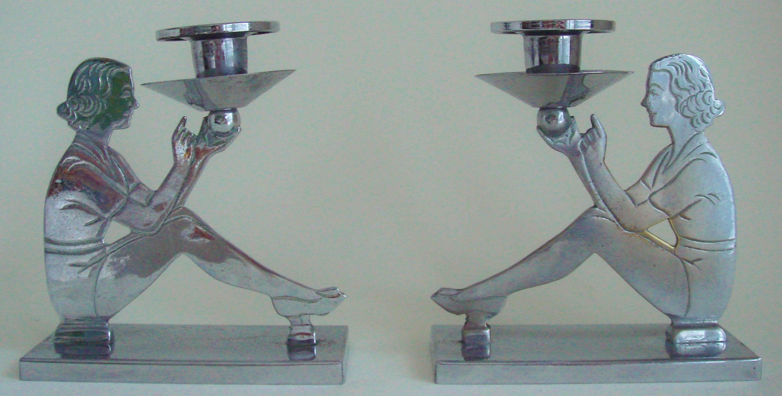 This pair of English Art Deco chrome-plated candlesticks each feature a silhouette of a seated young lady dressed in sporty attire with their features and costume details incised to both the front and back faces. Sitting on rectangular bases, each