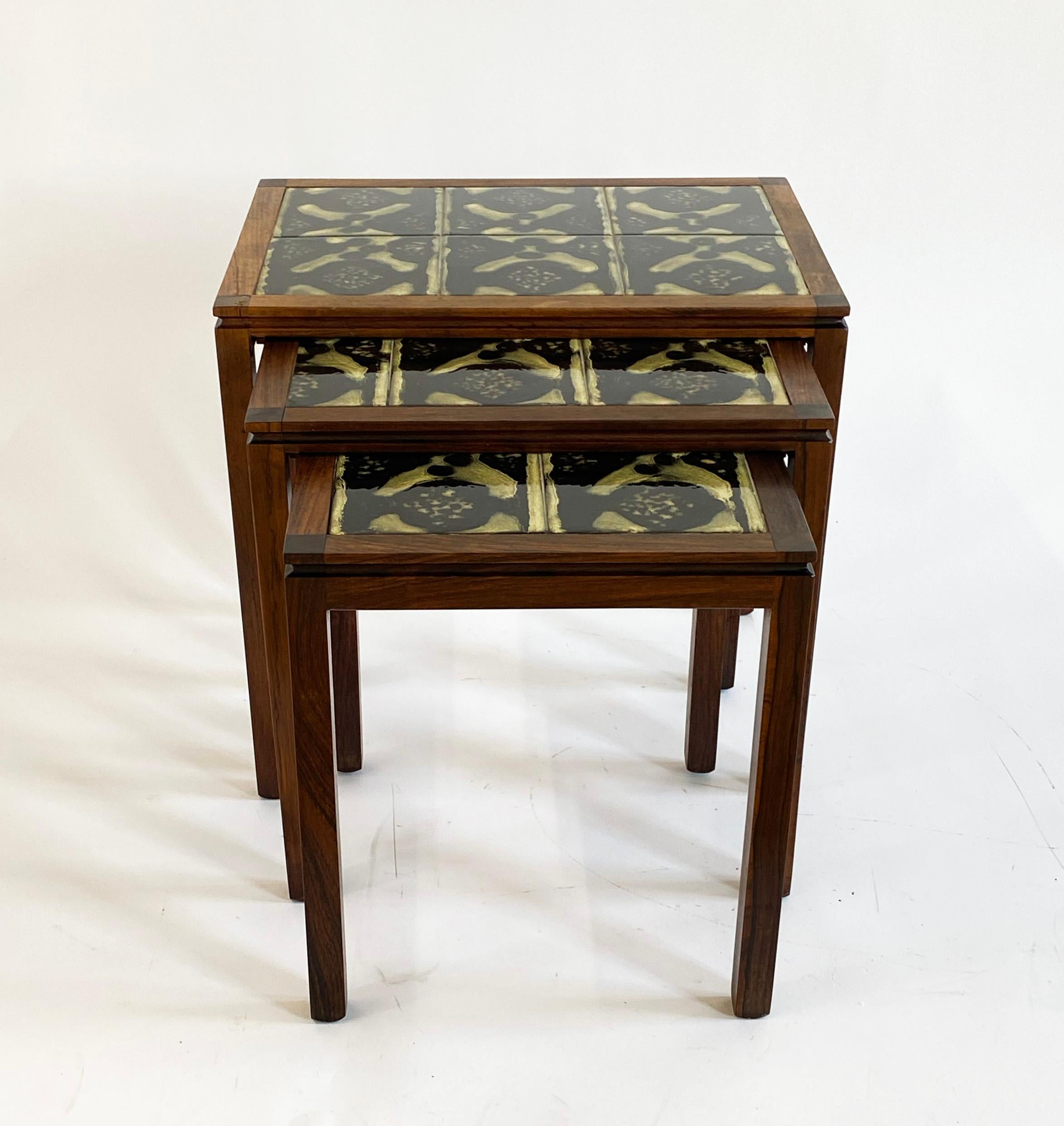 Here is a handsome set of mid-century testing tables that were made in Denmark. The set of three is made of rosewood and have tile tops. Each table is illegibly stamped on the underside with the manufacturer or designer, although you can make out