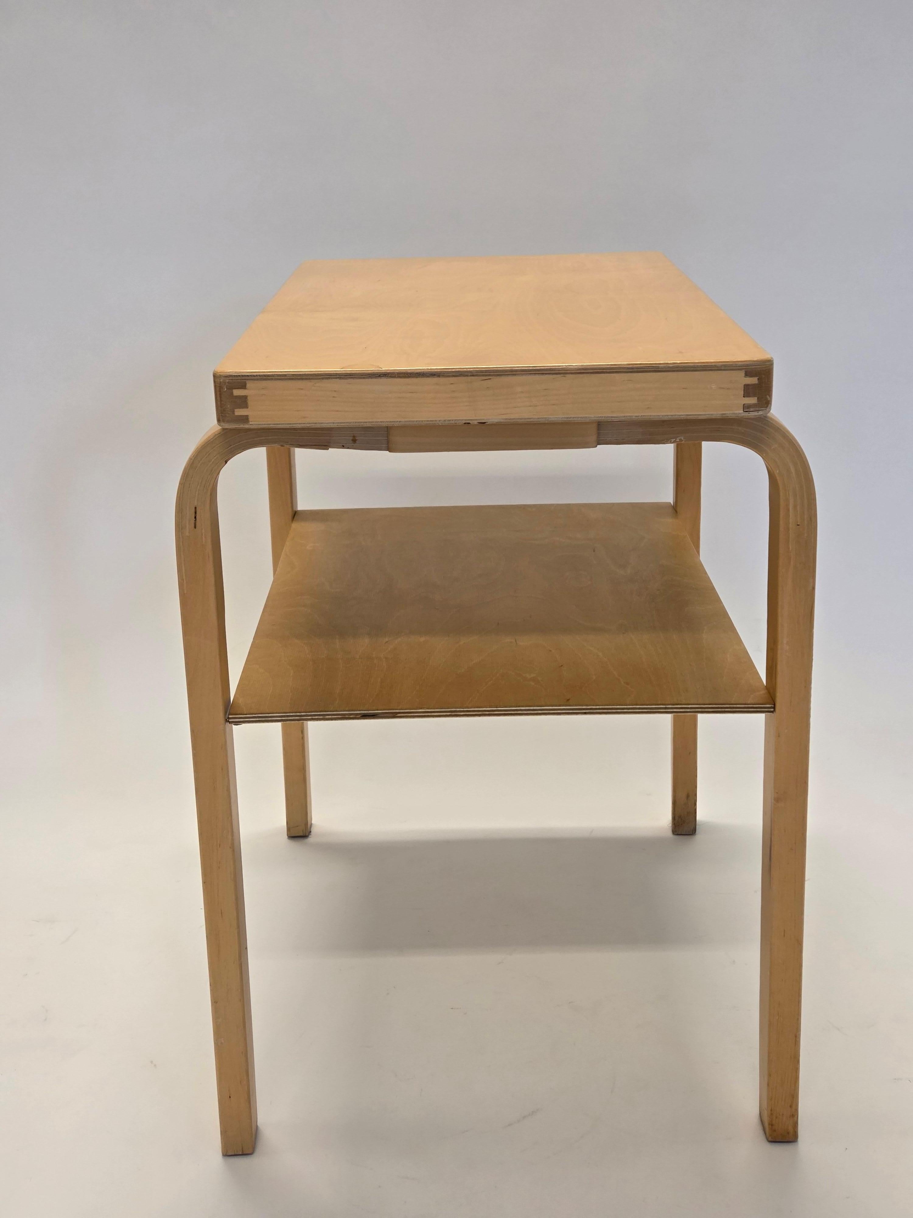An L-legged side table with two levels, designed by Alvar Aalto and manufactured by Artek. The table is from the 1950s-60s. The table has been restored and is in very good condition.