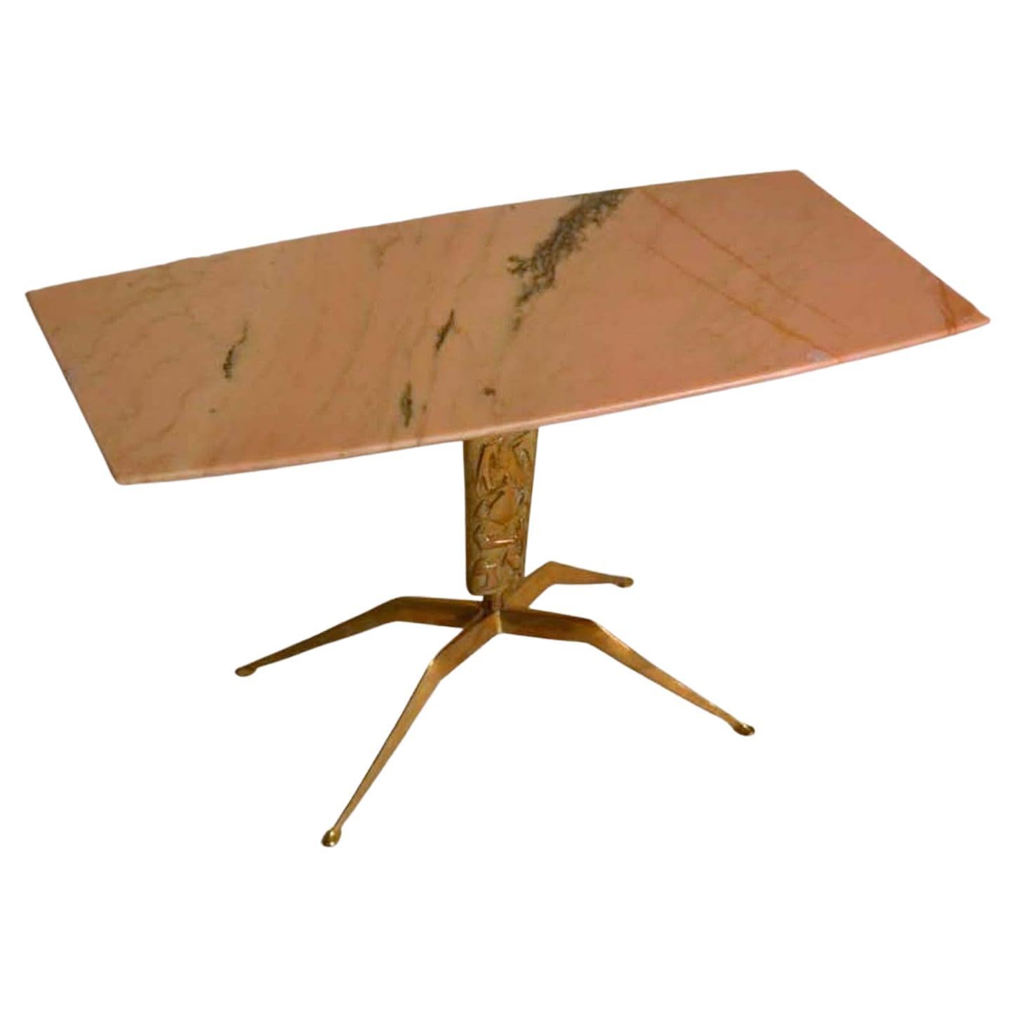 Rectangular coffee table with pink marble top with black veins supported by a sculpted cast brass base with a relief of figures and four spider legs on oval feet. The figures on the leg are abstracted in a typical 1950s style and tell the story of