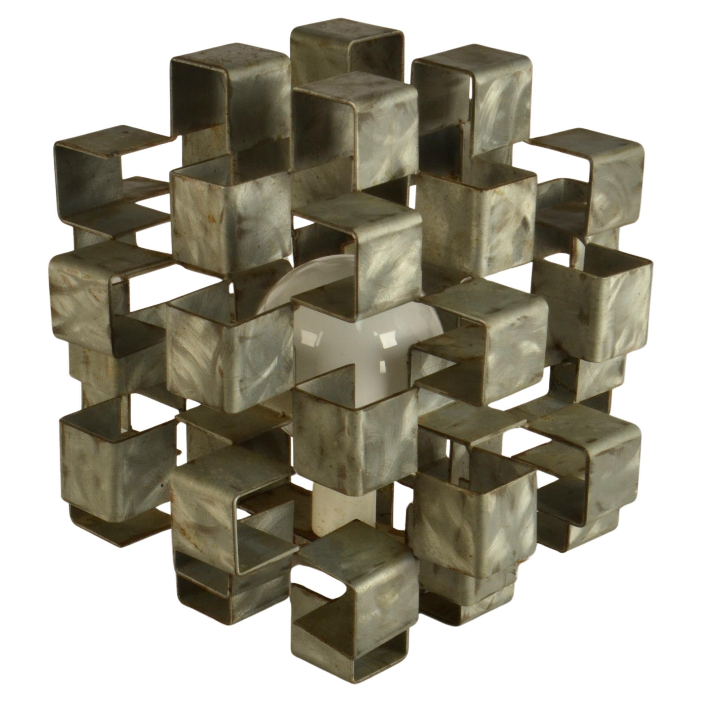 Lampe de table sculpturale en forme de cube construite en acier plié et zingué avec patine d'origine, Italie 1960's. Il révèle la lumière par segments entre les structures métalliques. 
Il s'agit d'un objet lumineux unique fabriqué par un artiste